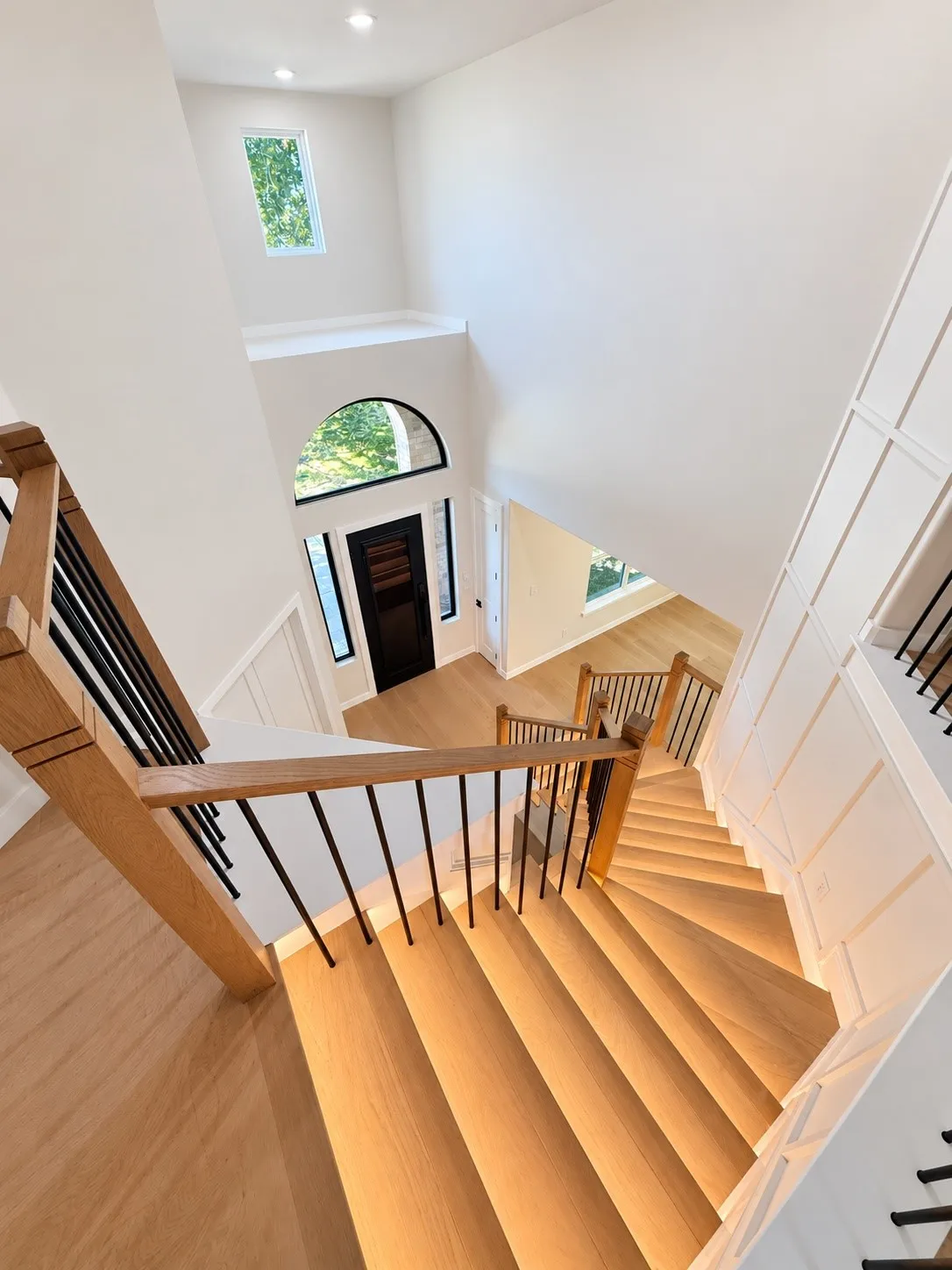 Grand entryway with a two-story ceiling, arched transom window, wood-finish flooring, and a staircase featuring wood railings and wrought iron spindles