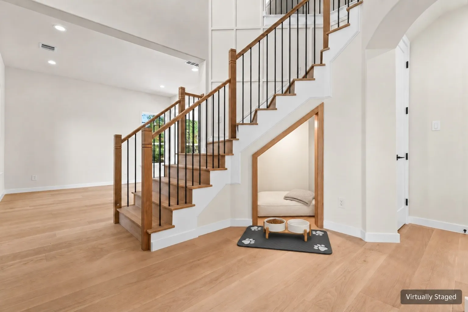 Hardwood staircase with black iron spindles, light wood-finish flooring, recessed lighting, and an arched doorway