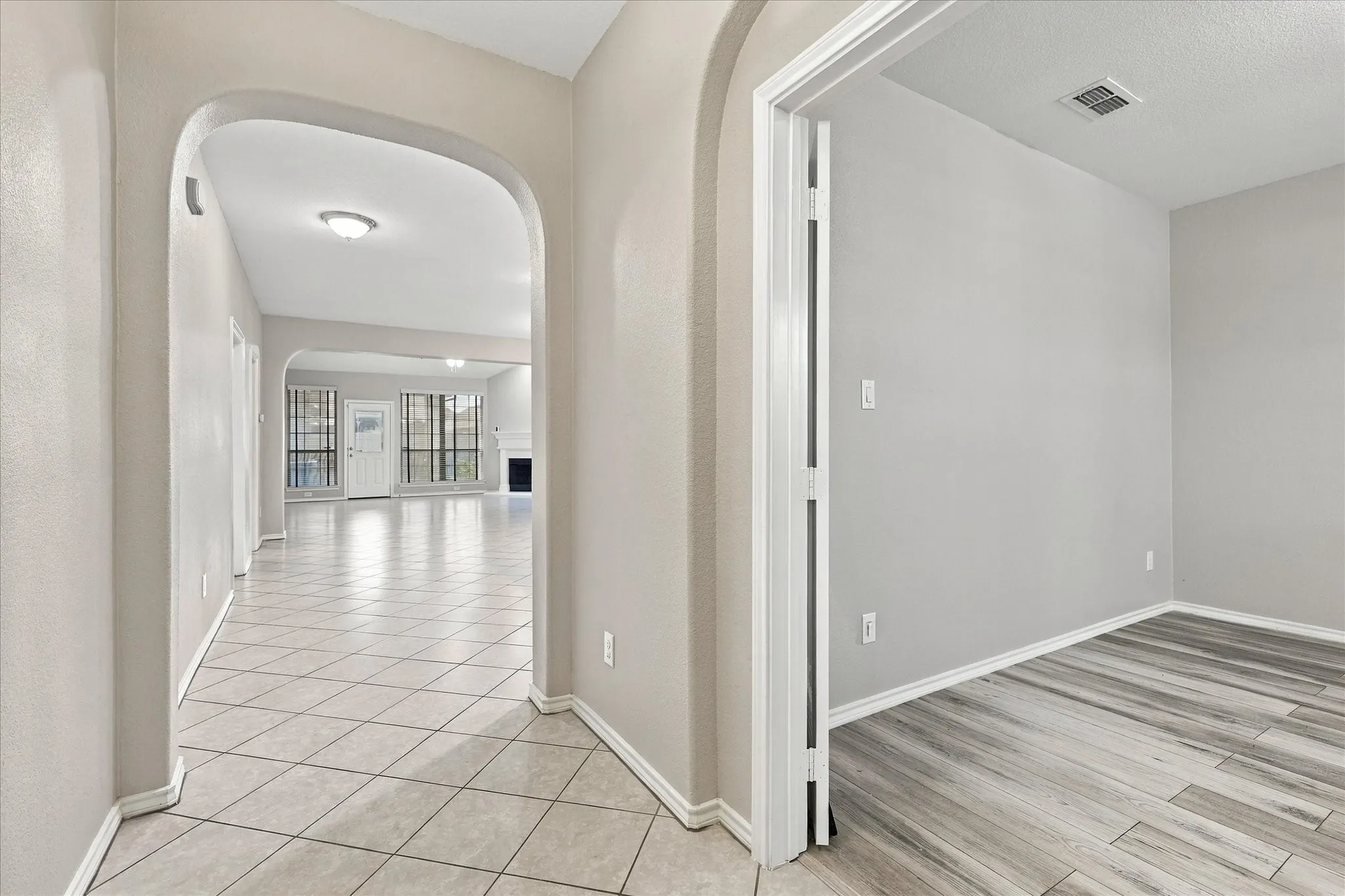 Arched entryways delineate spaces, with tile flooring leading into a room featuring wood-finish flooring