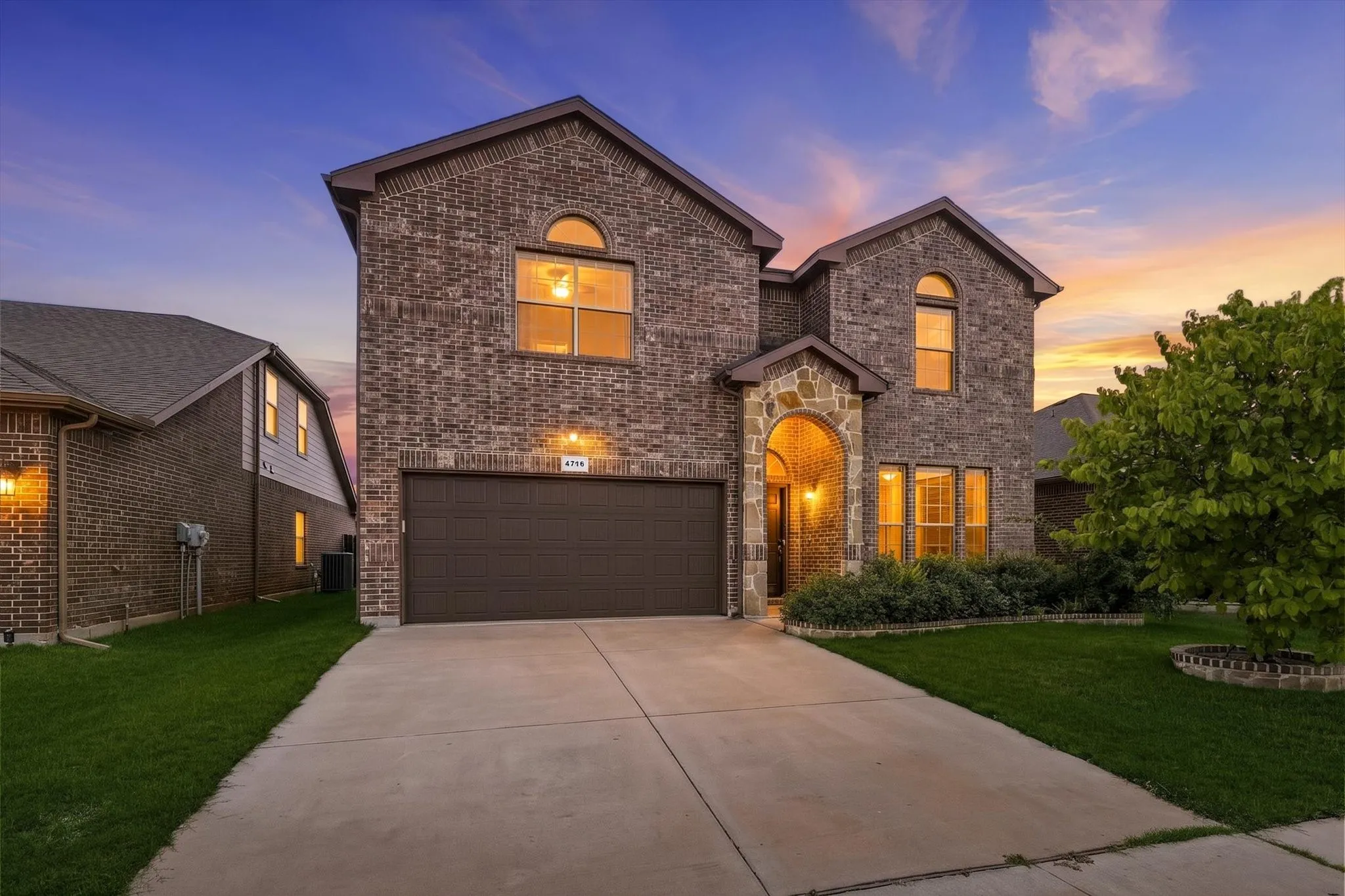 Brick exterior with stone accents, arched entryway, attached garage, and landscaped front yard