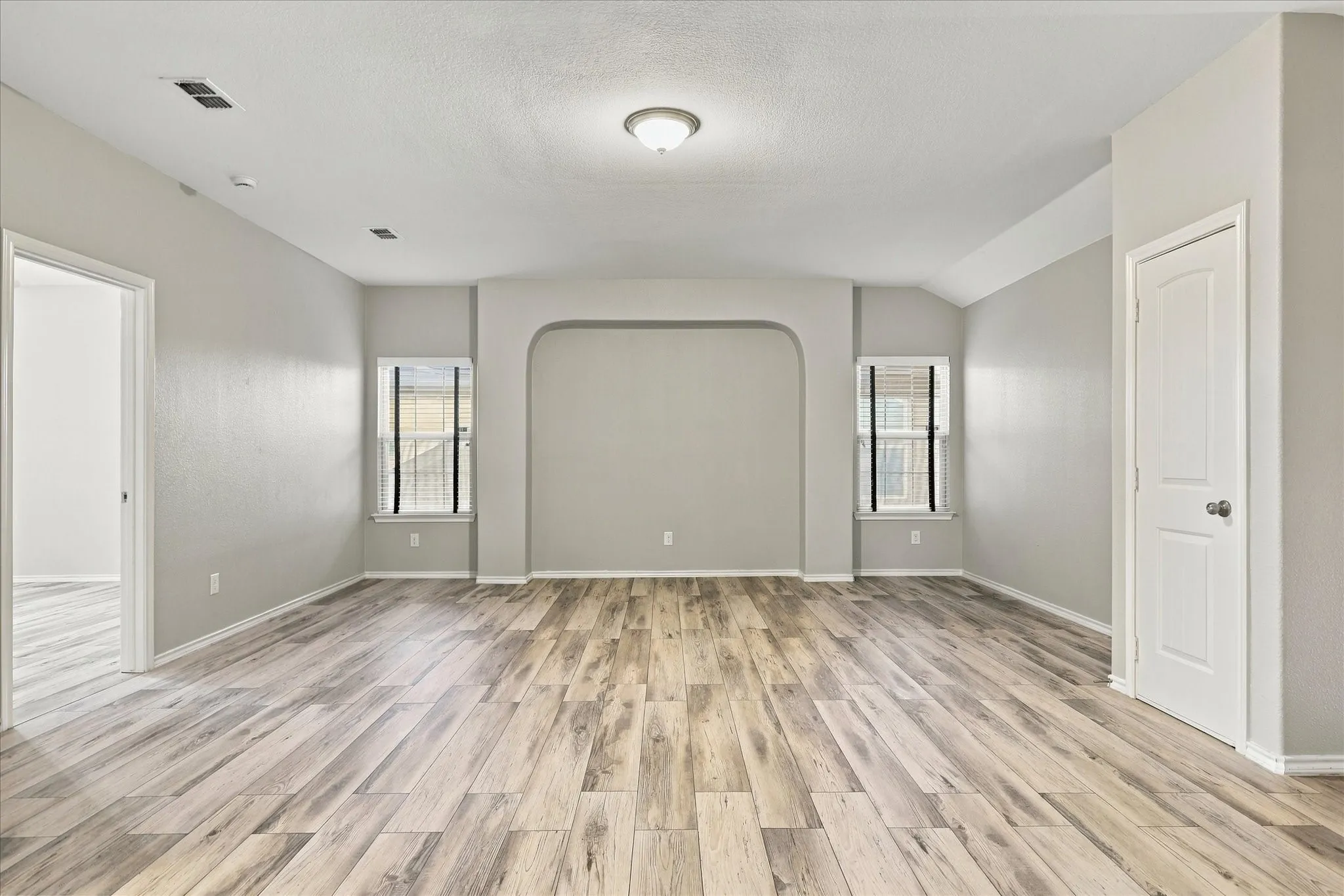 Wood-finish flooring, recessed archway, two windows with sills, white interior doors, and a ceiling-mounted light fixture