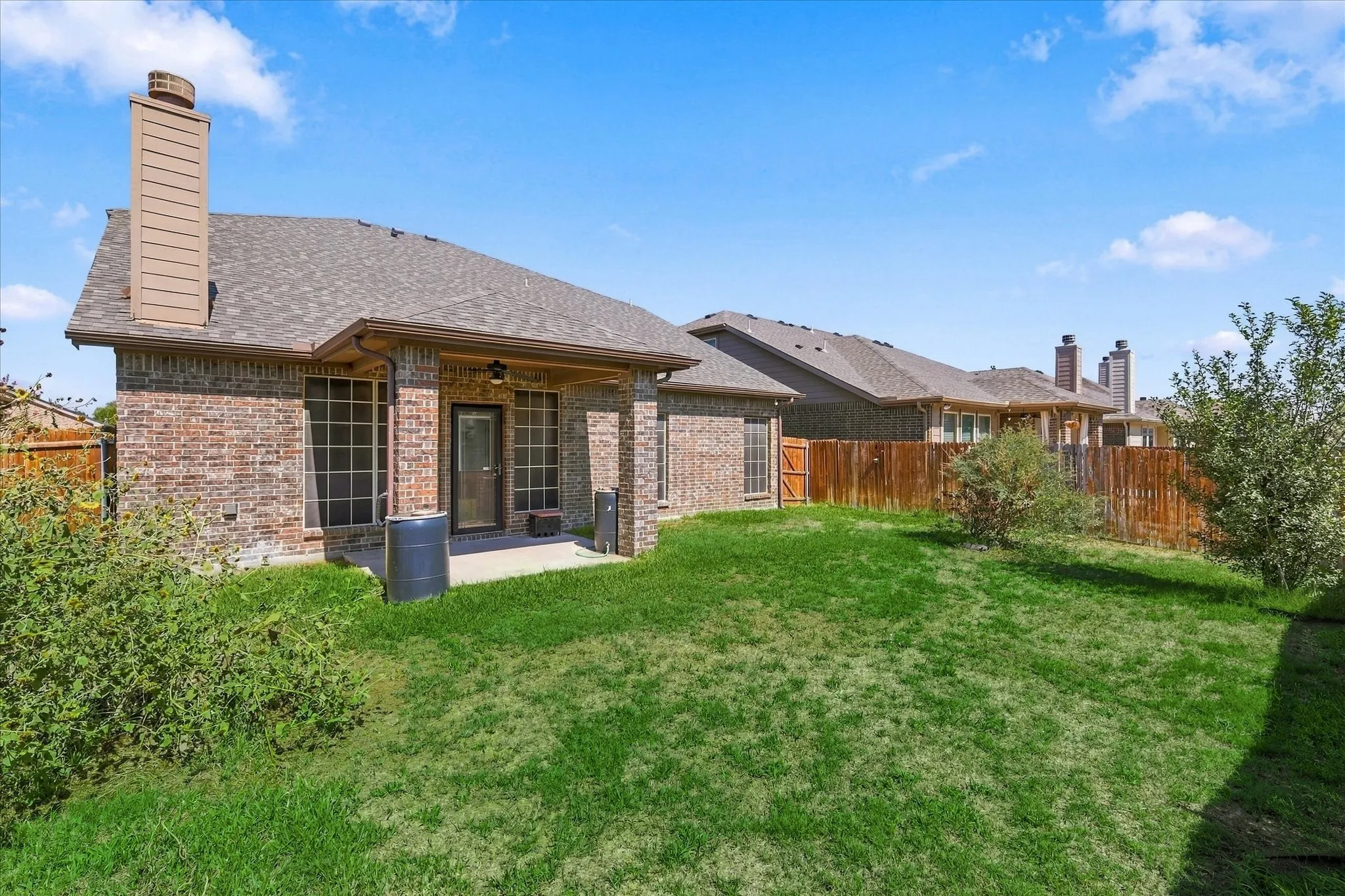 Backyard featuring a brick exterior, covered patio, privacy fence, and manicured lawn