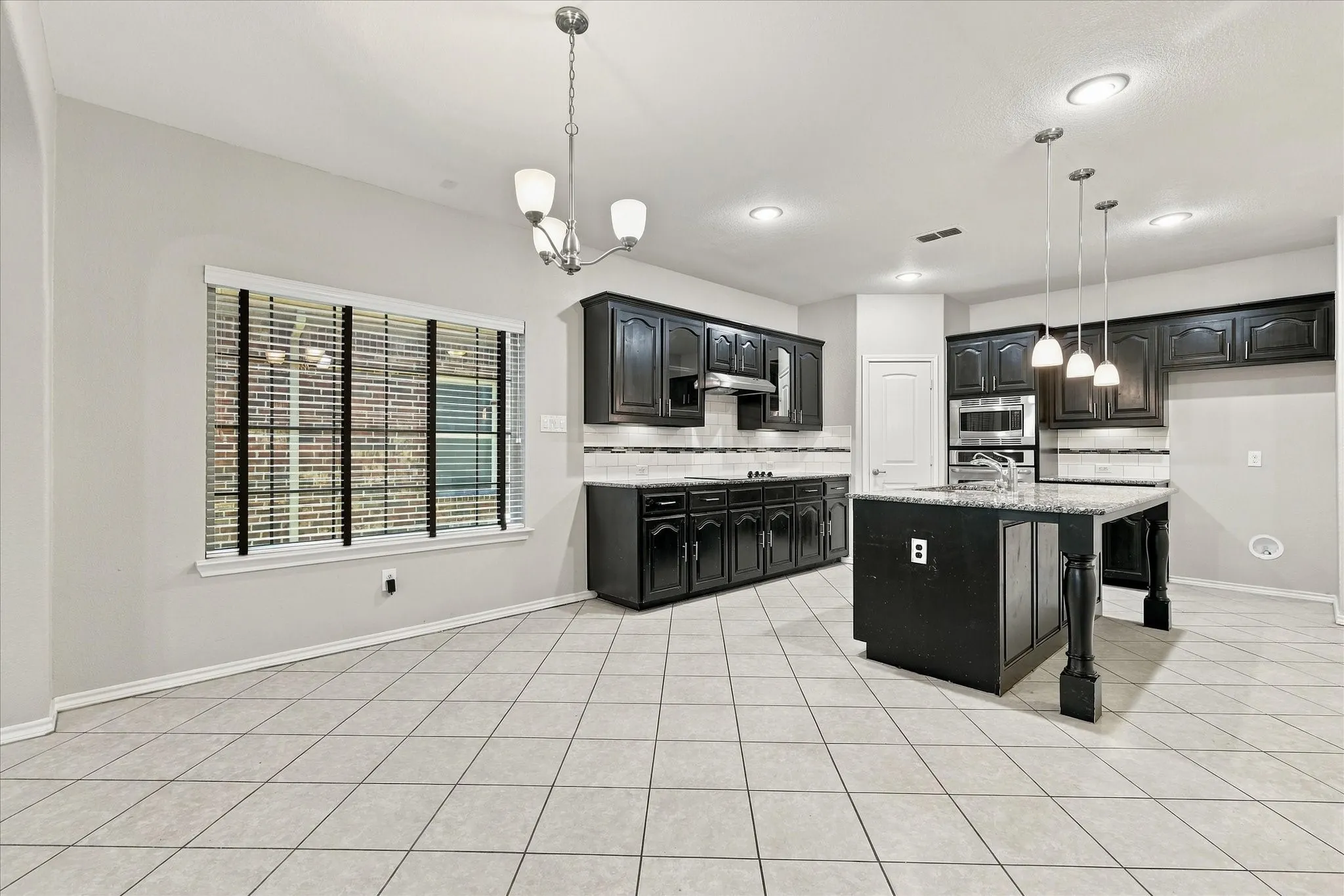 Kitchen featuring black cabinetry, light-toned tile flooring, recessed lighting, a center island with pendant lighting, and stainless steel appliances