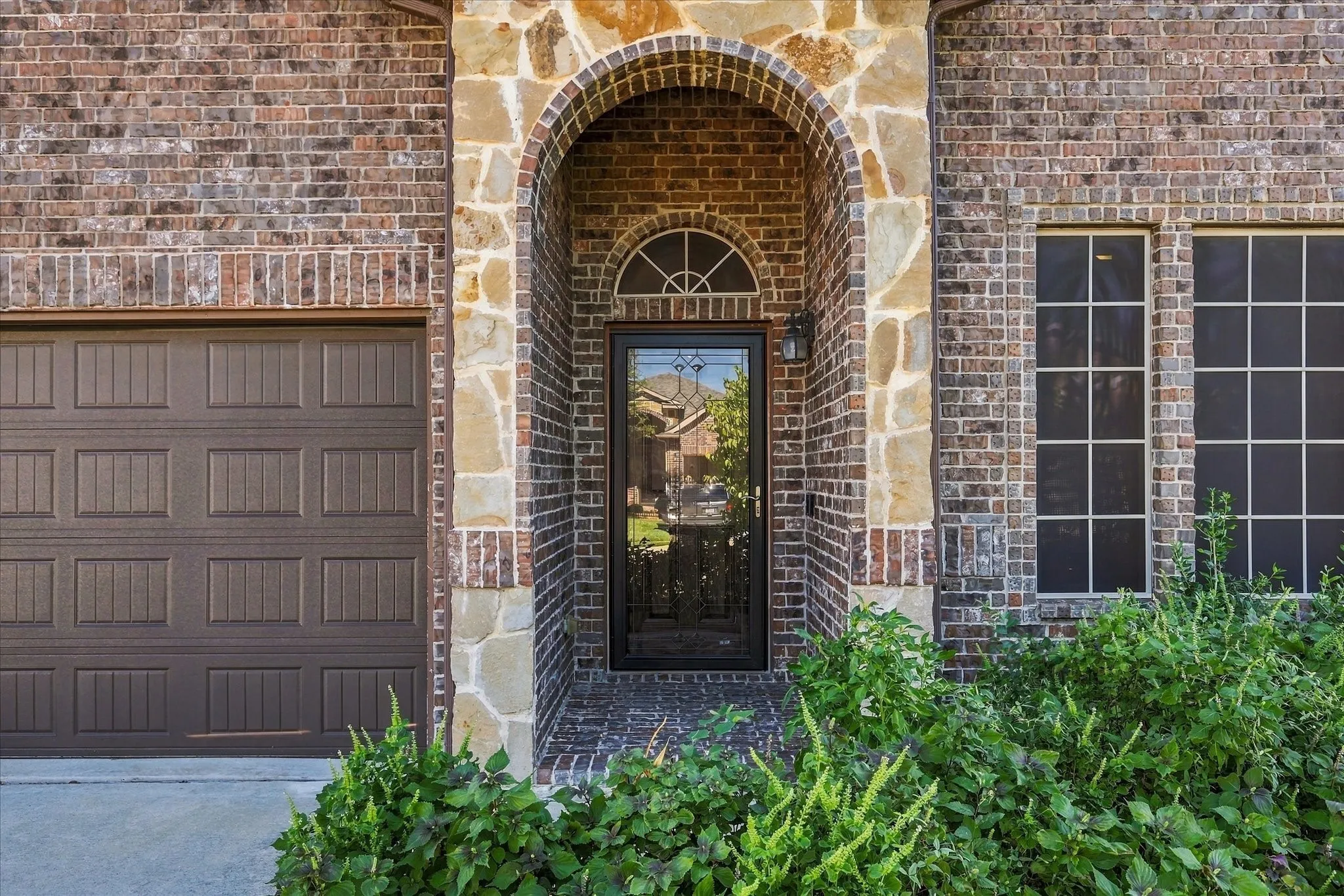 Brick and stone exterior featuring an arched entry, a paneled garage door, and multiple windows with grilles