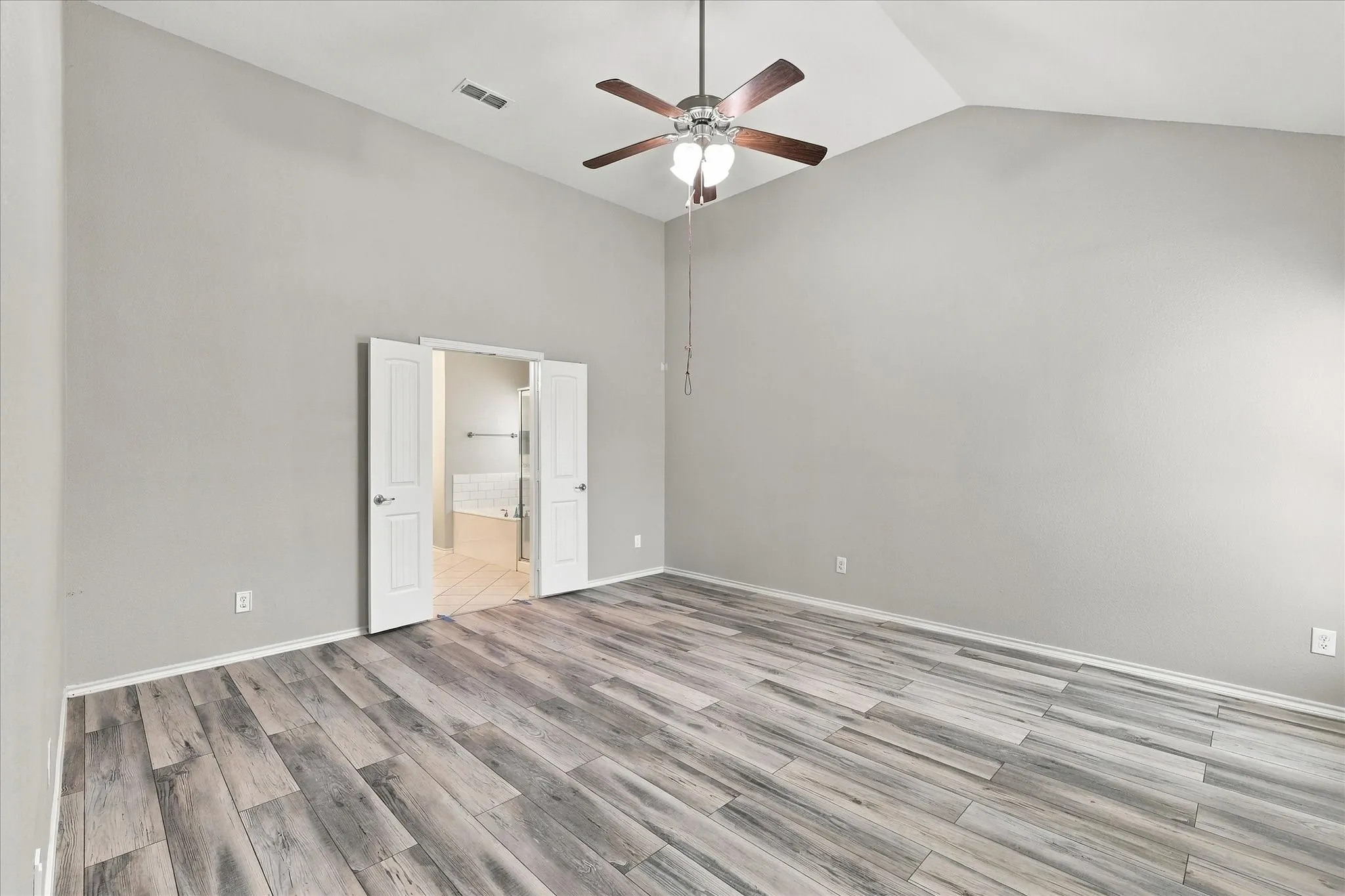 Vaulted ceiling with a ceiling fan, wood-finish flooring, and double doors opening to a bathroom with a built-in tub and a shower enclosure