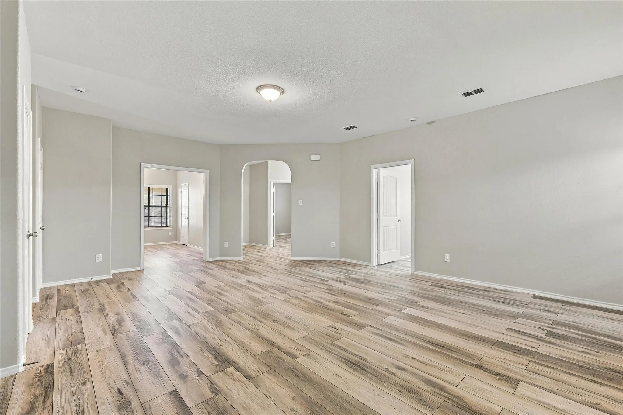Wood-finish flooring, light gray wall paint, white trim, recessed lighting, and arched doorways