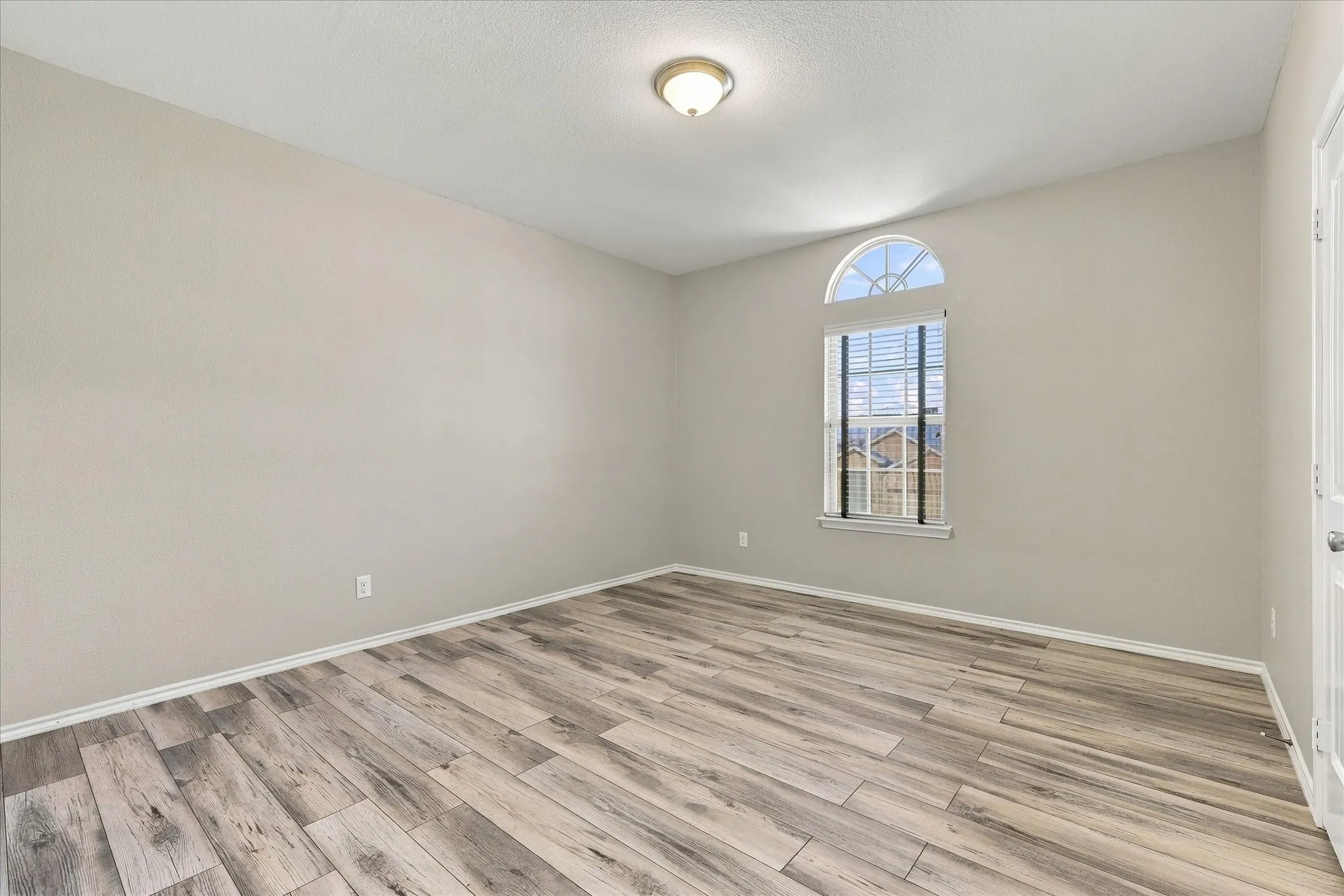 Wood-finish flooring, neutral wall color, and arched window with blinds