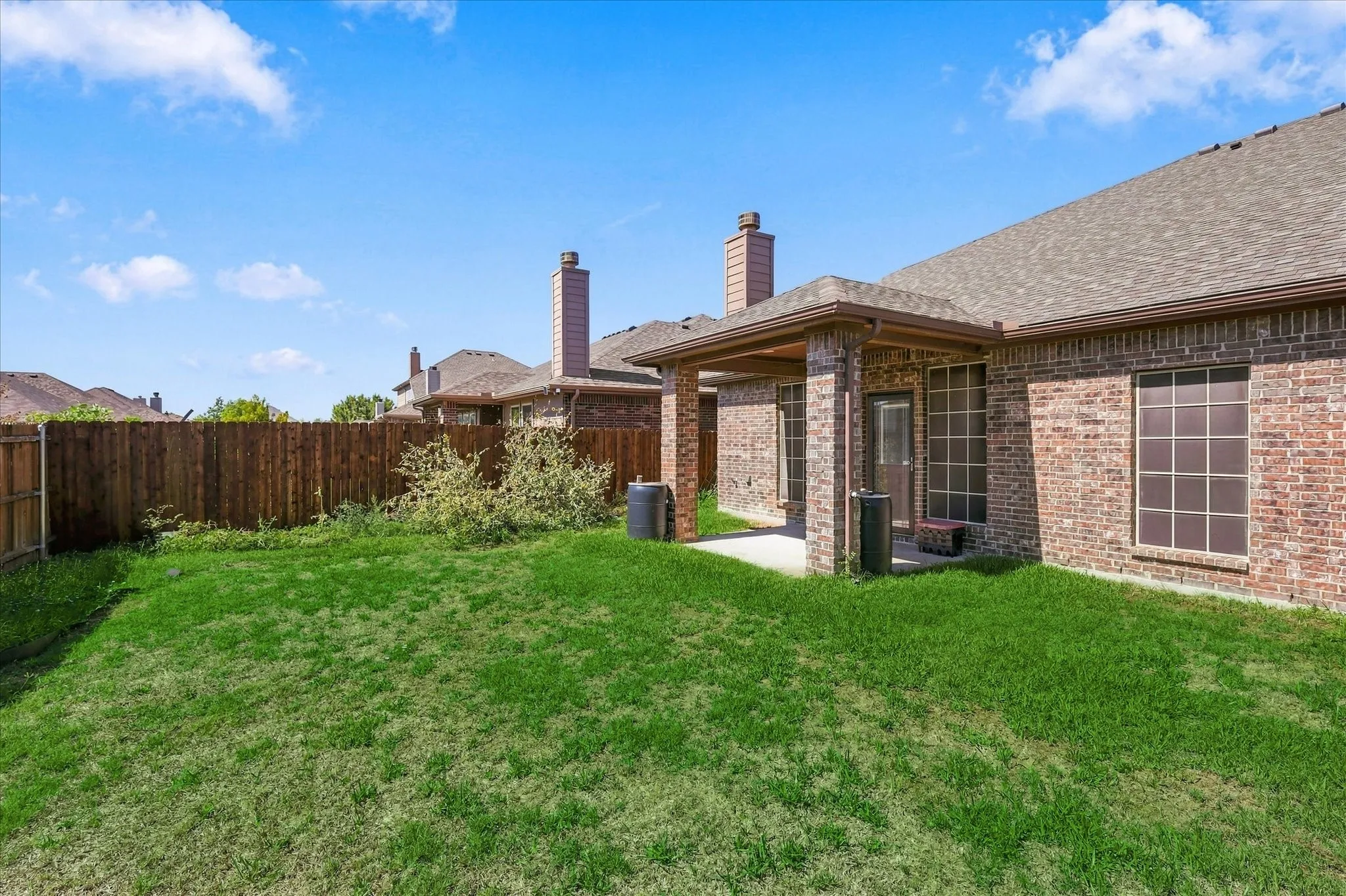 Expansive green yard with a covered patio, brick exterior, and a privacy fence