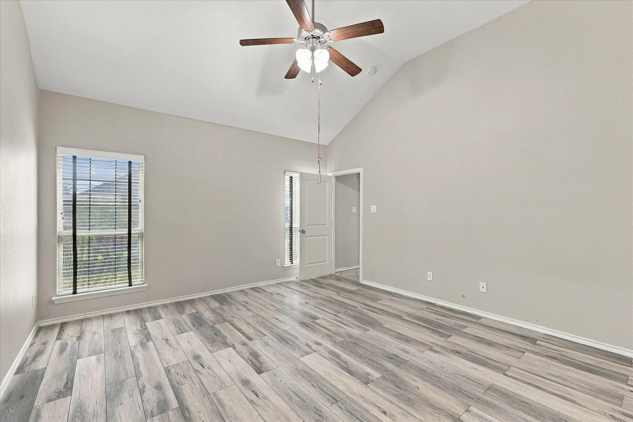 Vaulted ceiling, wood-finish flooring, ceiling fan, and window with blinds