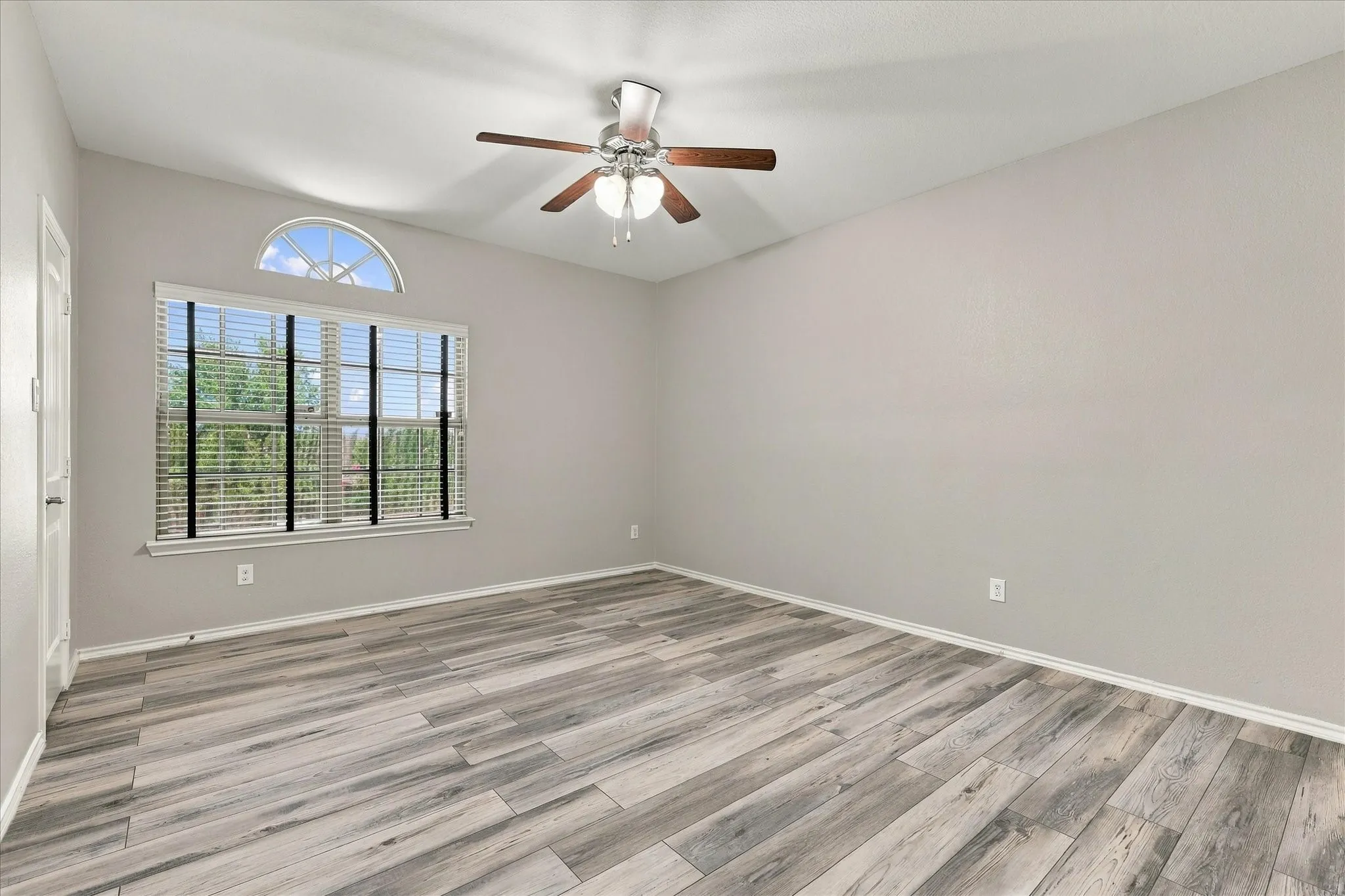 Vaulted ceiling with a ceiling fan, wood-finish flooring, and a large window with an arched transom
