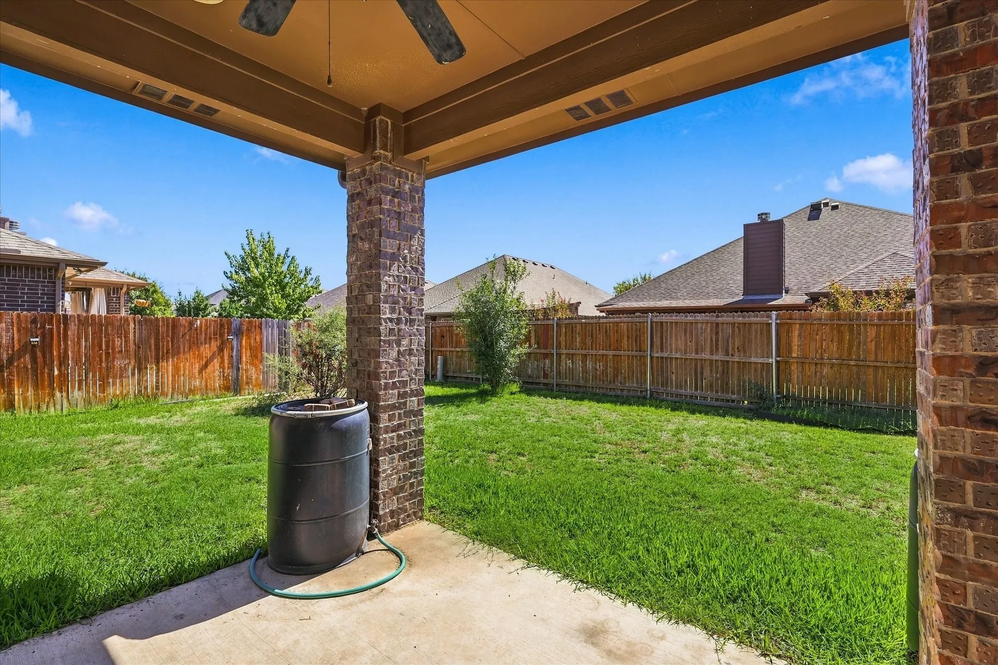 Covered patio with a ceiling fan, concrete flooring, and brick-clad support columns