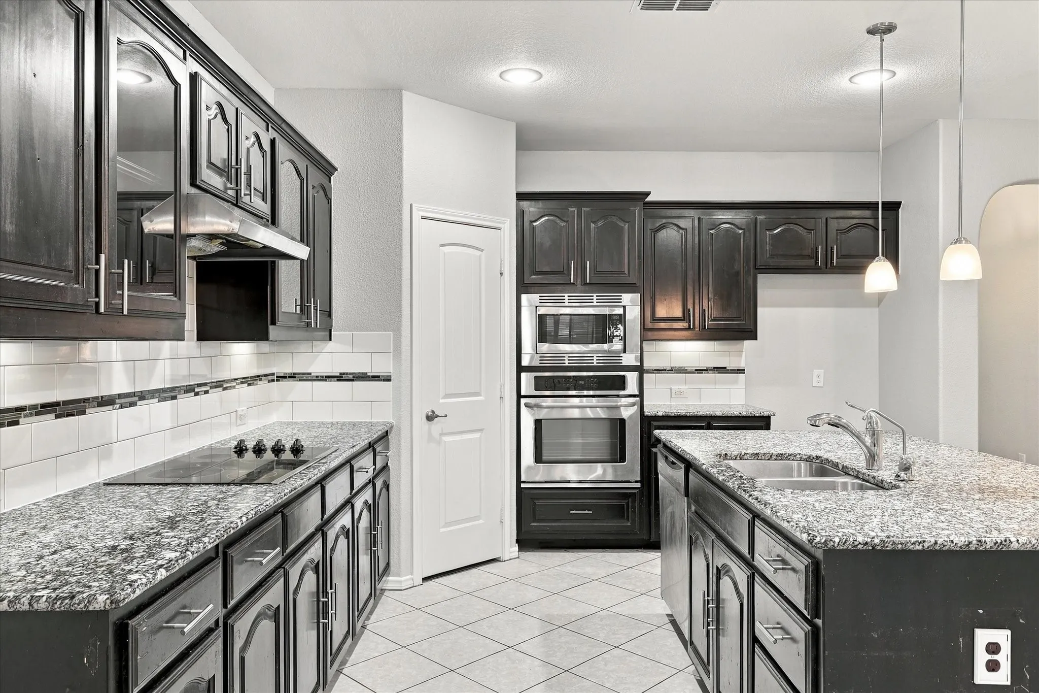 Kitchen featuring dark wood cabinetry, granite countertops, tile flooring, stainless steel appliances, and an undermount sink