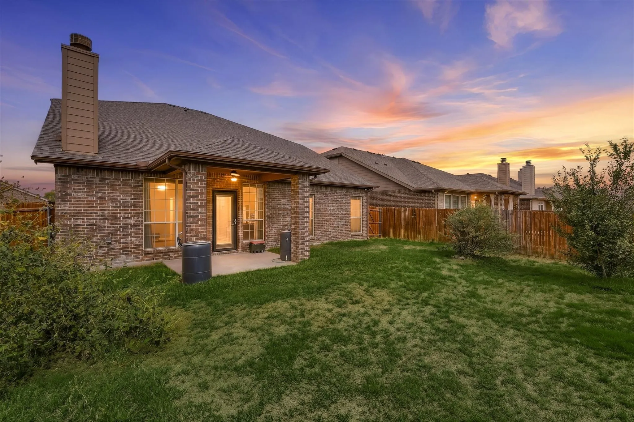 Brick exterior with multiple windows, covered patio, and shingled roof