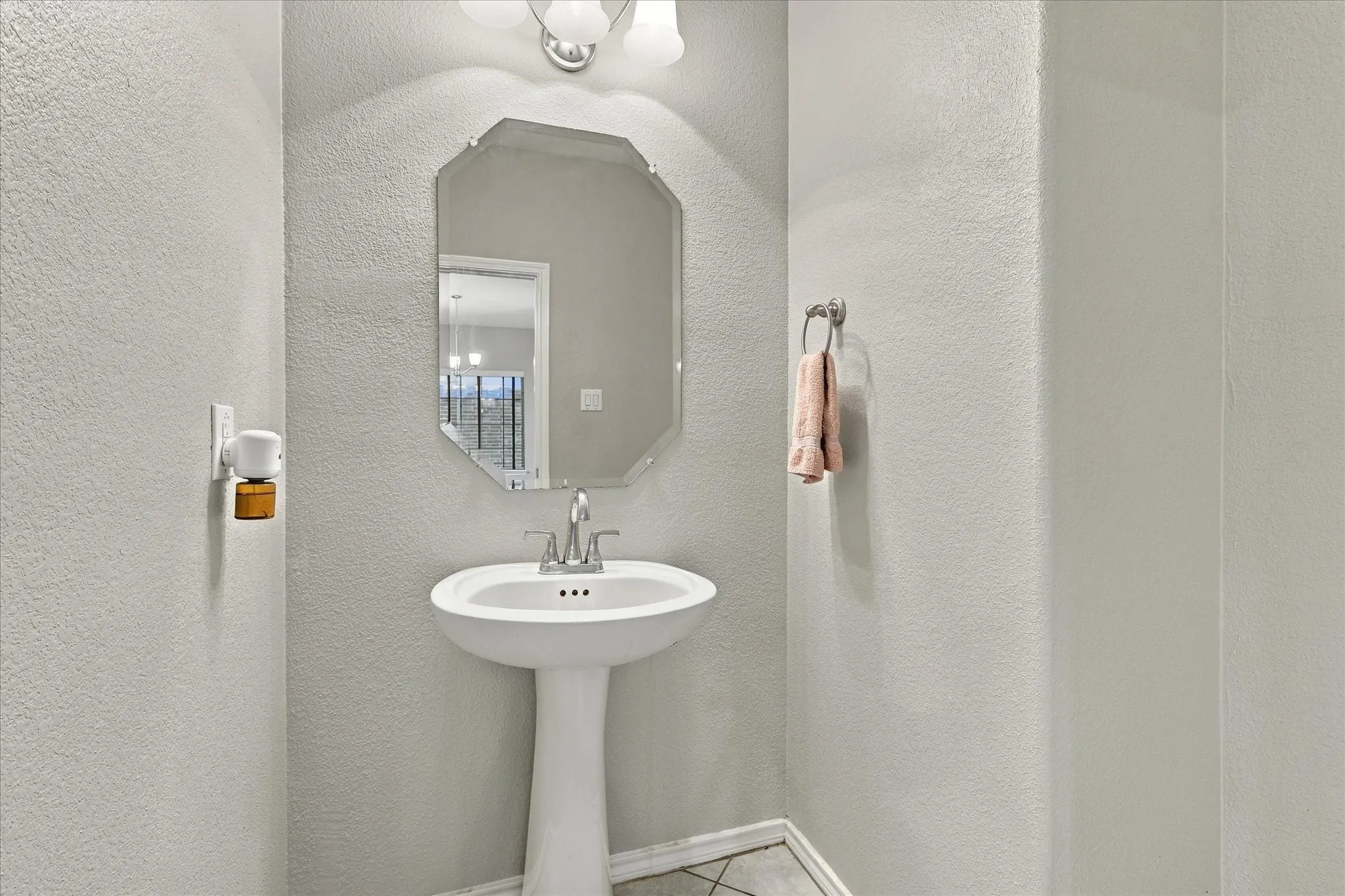 Pedestal sink with chrome faucet, octagonal mirror, and overhead vanity lighting