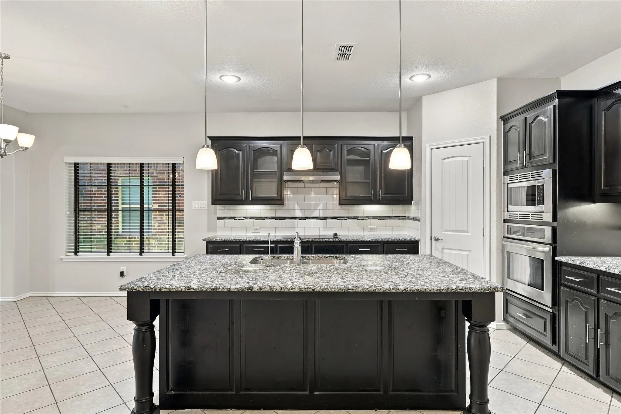 Kitchen featuring an island with a stone-finish countertop, dark wood-finish cabinetry, stainless steel appliances, and tile flooring