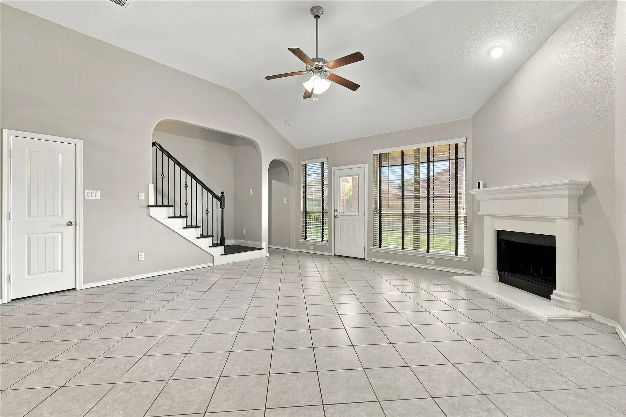 Vaulted ceiling with a ceiling fan, tiled flooring, built-in fireplace, and a staircase with wrought iron balusters