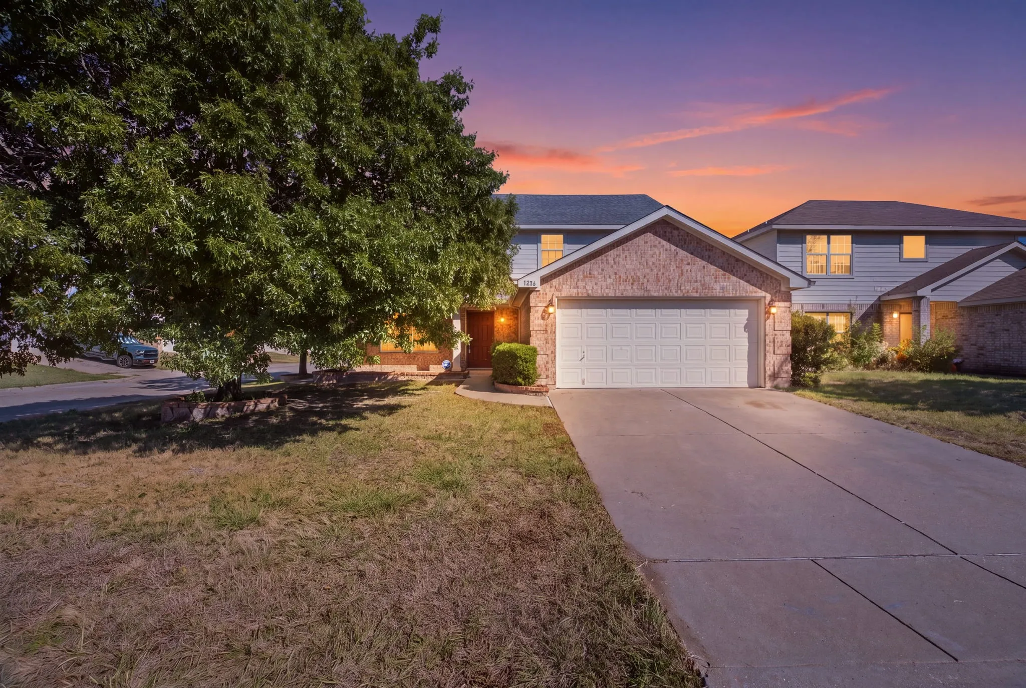 Brick facade with a prominent garage, a concrete driveway, and a large front tree