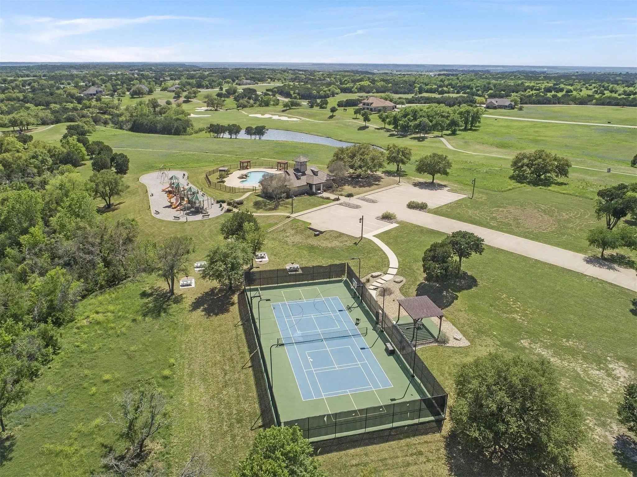 Tennis court with surrounding fencing, adjacent covered seating area, and paved pathways