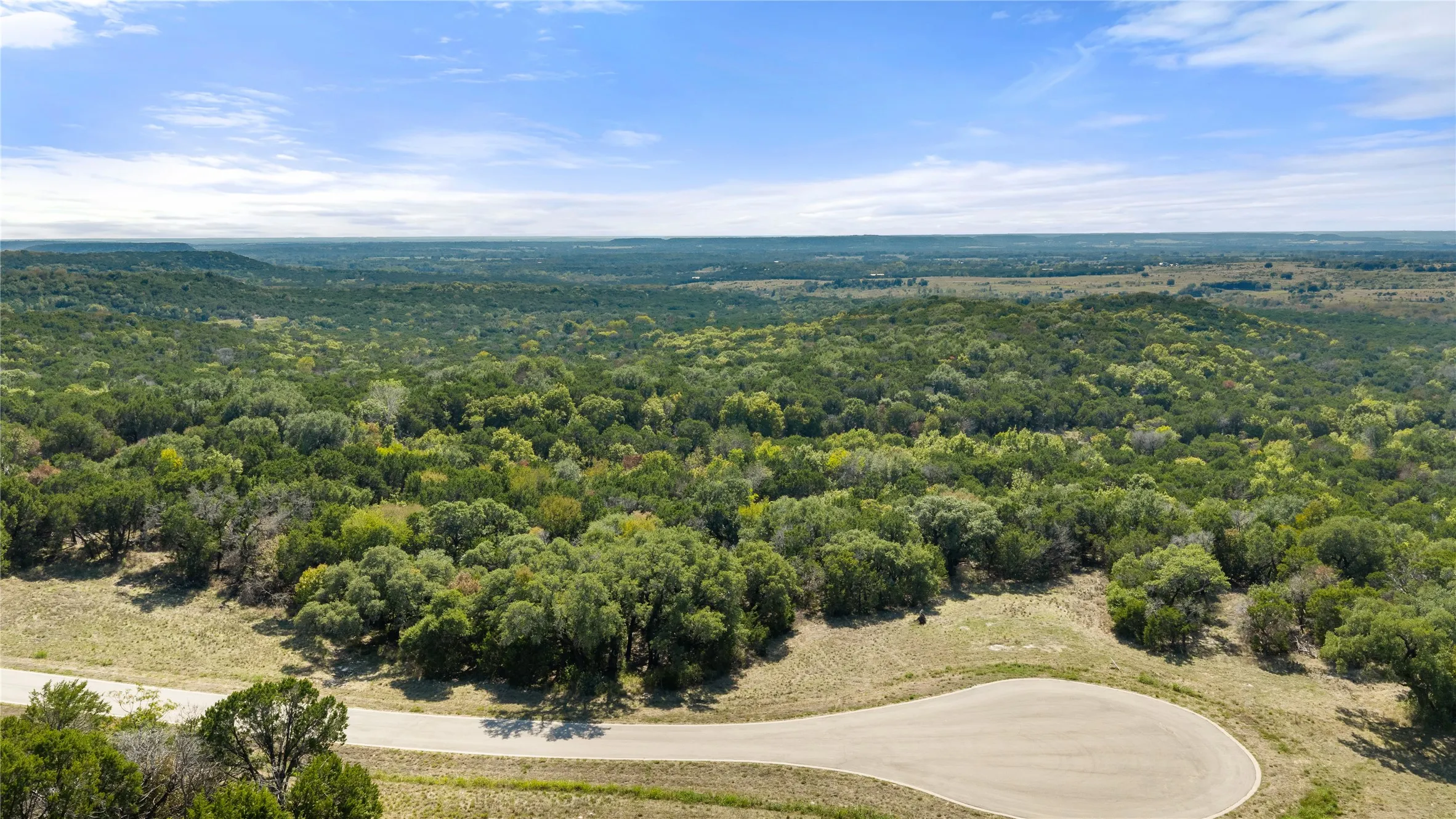 Sprawling rural property showcasing lush tree-lined acreage, mature oak and cedar specimens, natural water features including a meandering creek, and rolling topography with cleared pasture land