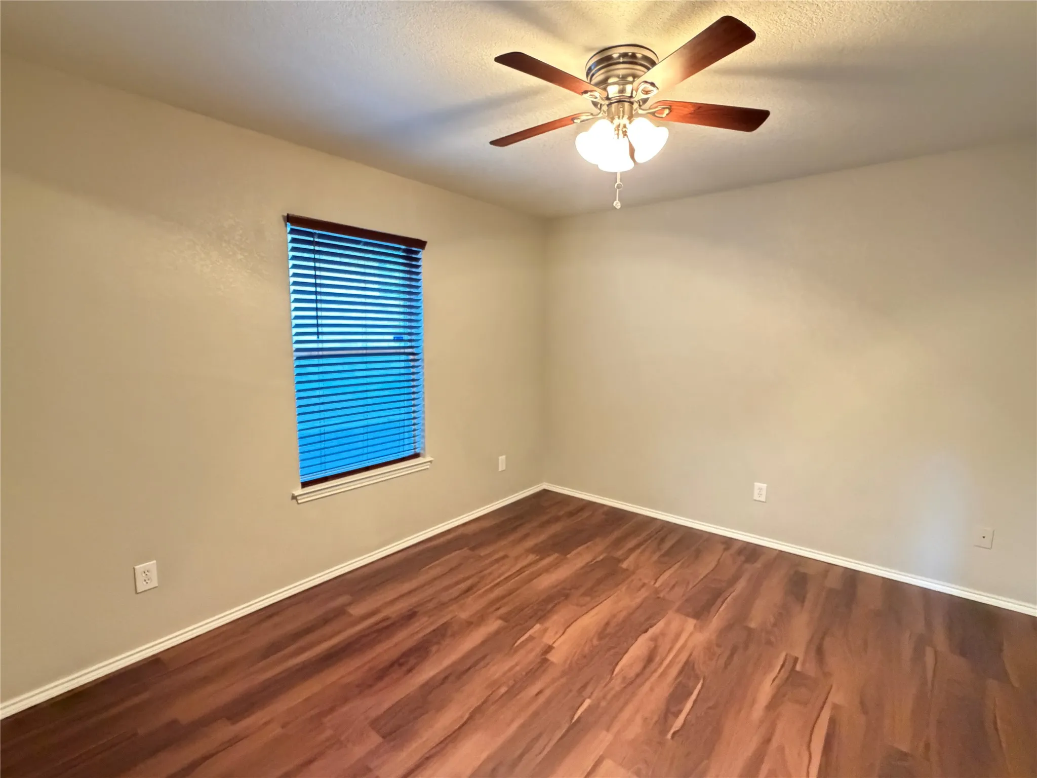 Wood-finish flooring with white trim, window with blinds, and a ceiling fan with integrated lighting