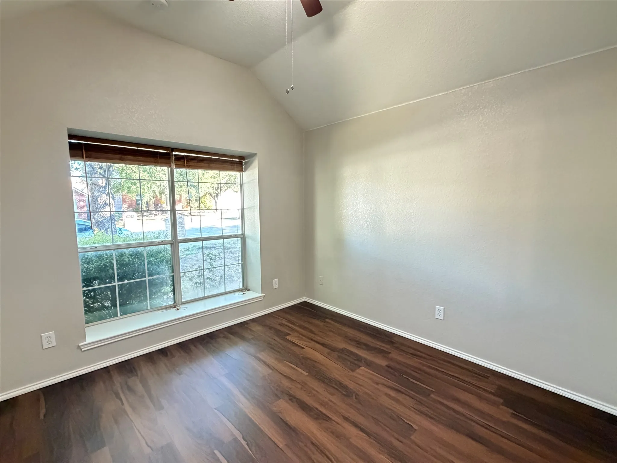 Vaulted ceiling, wood-finish flooring, large window, ceiling fan, and neutral wall tones
