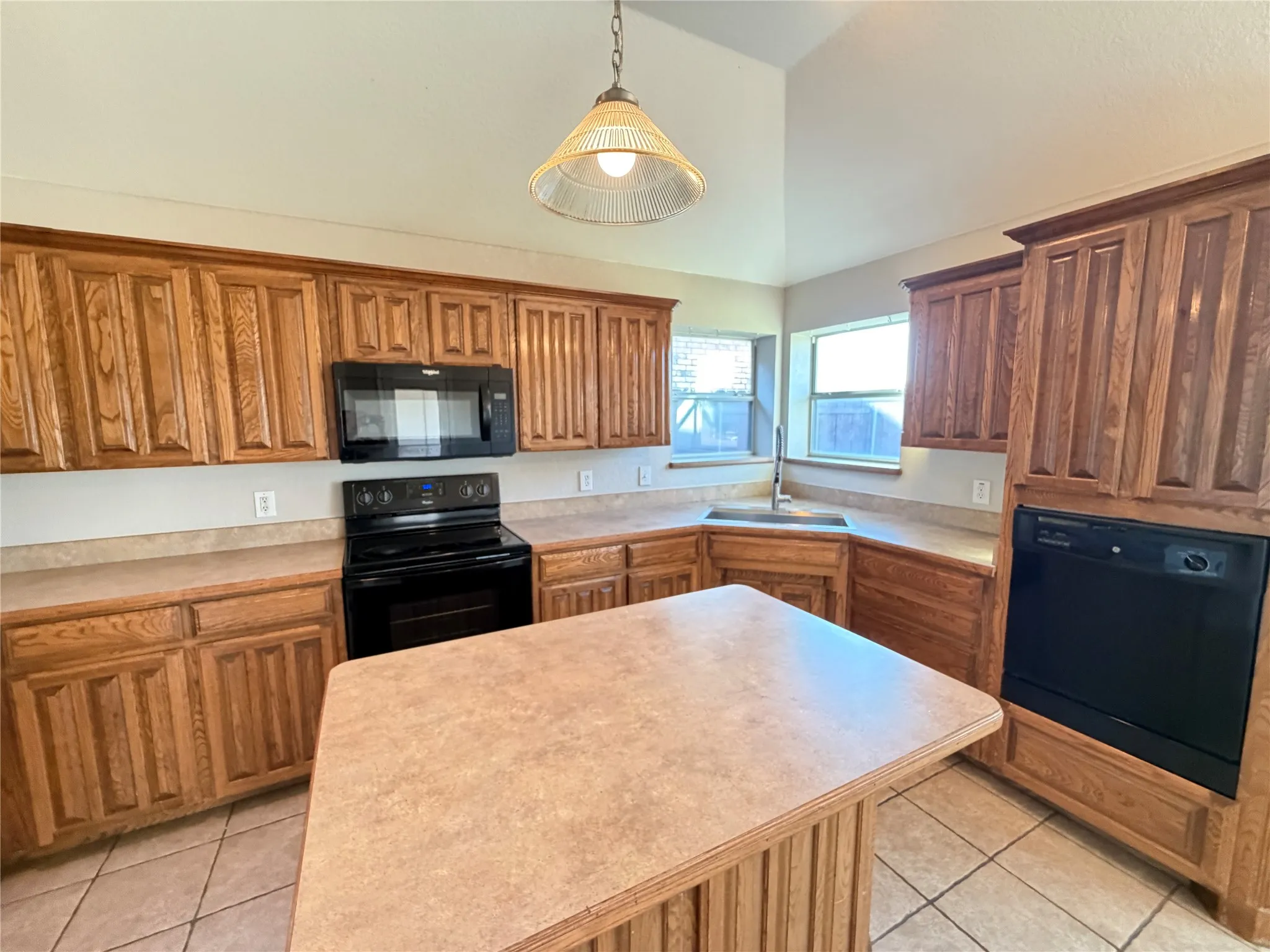 Kitchen featuring wood cabinetry, black appliances, a central island, and vaulted ceilings