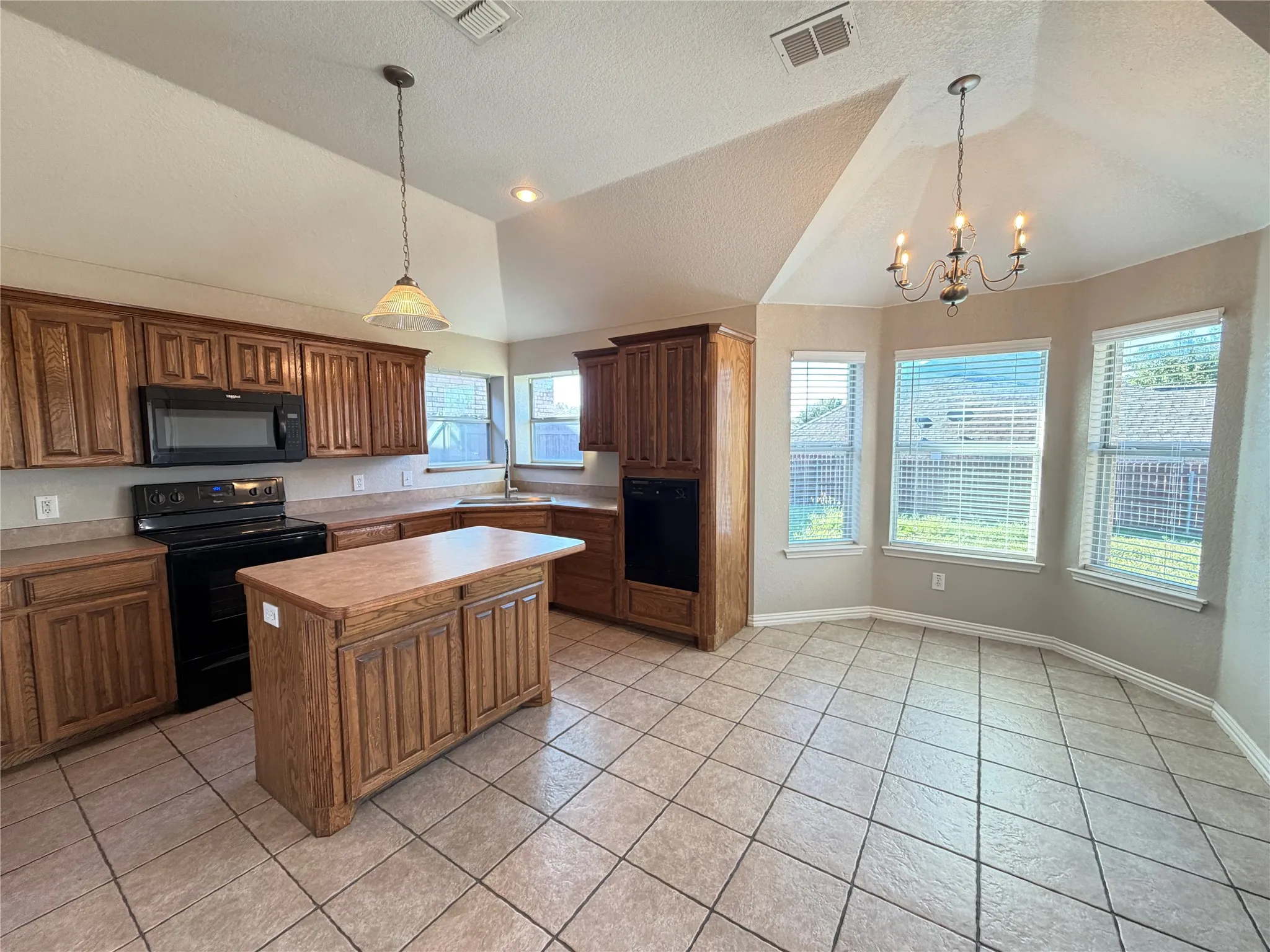 Kitchen featuring wood cabinetry, a central island, black appliances, and neutral countertops