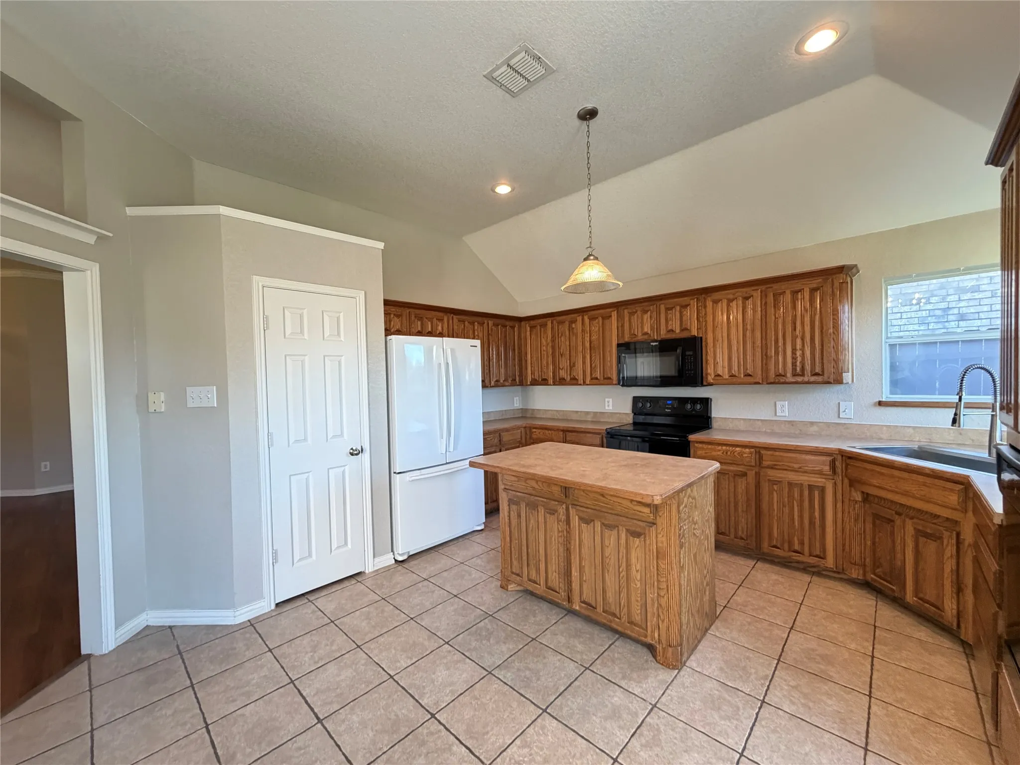 Kitchen featuring a vaulted ceiling, recessed lighting, a central island, wood-finish cabinetry, and tiled flooring