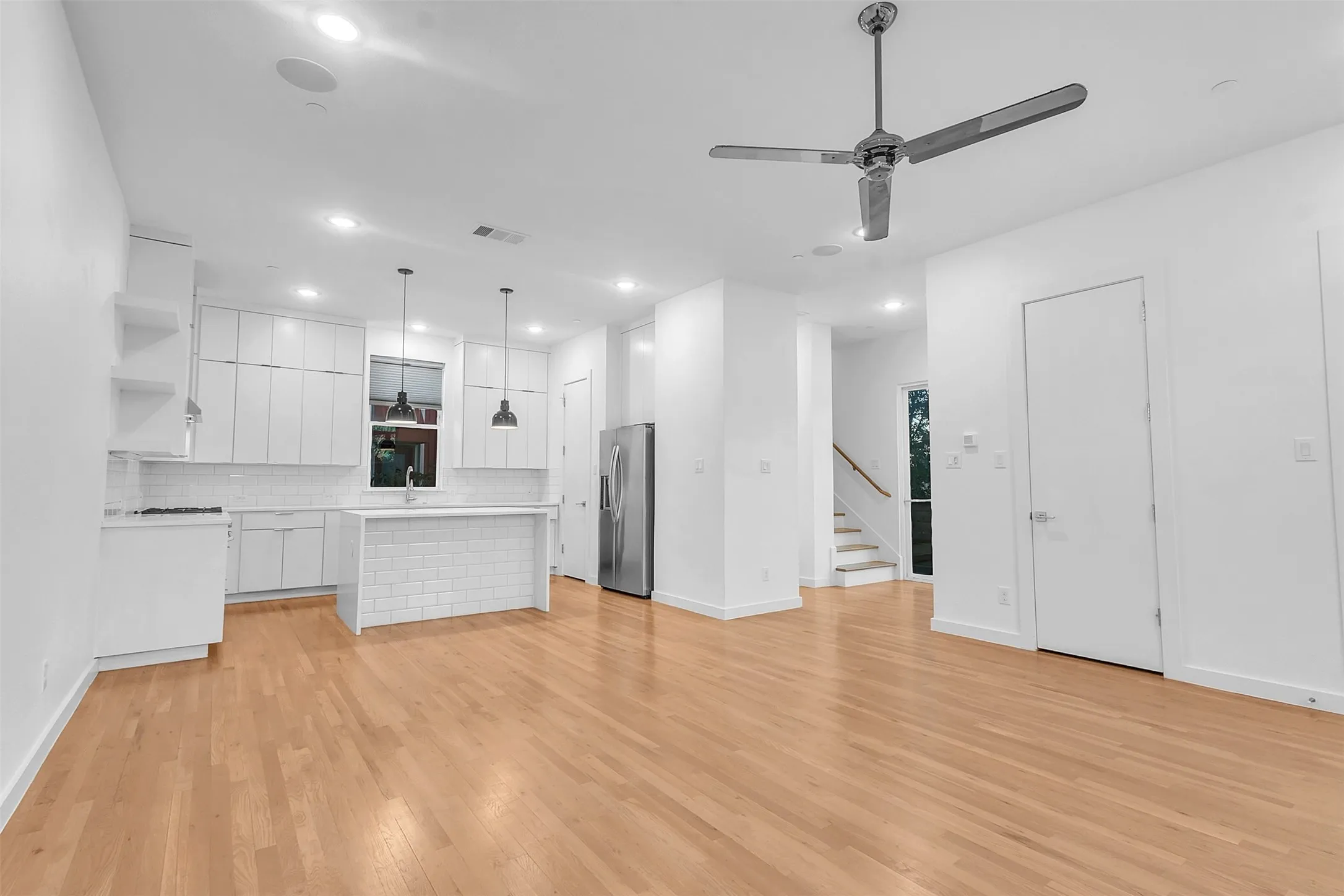 Open living and kitchen area in this Dallas condo with wood-look floors, chrome ceiling fan, ceiling speakers and stairs