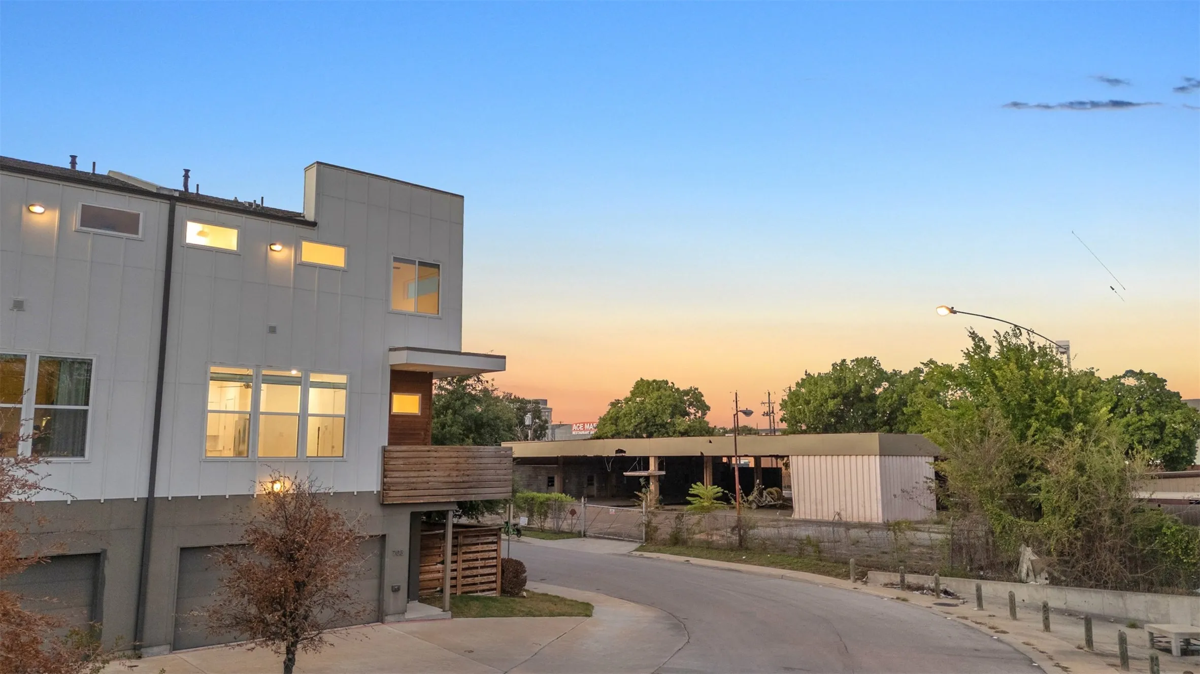 Dusk view of this East Dallas condo's corner end unit with a wood balcony, lit windows and the curving side street