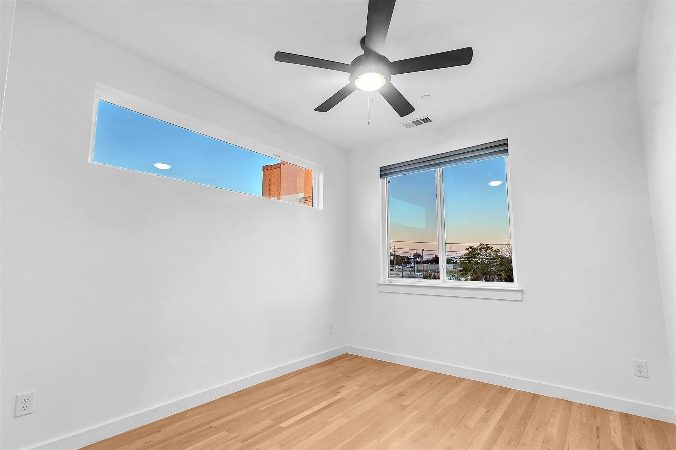 Bedroom with wood-look floors, a ceiling fan with light, a long transom window and a second window with shade