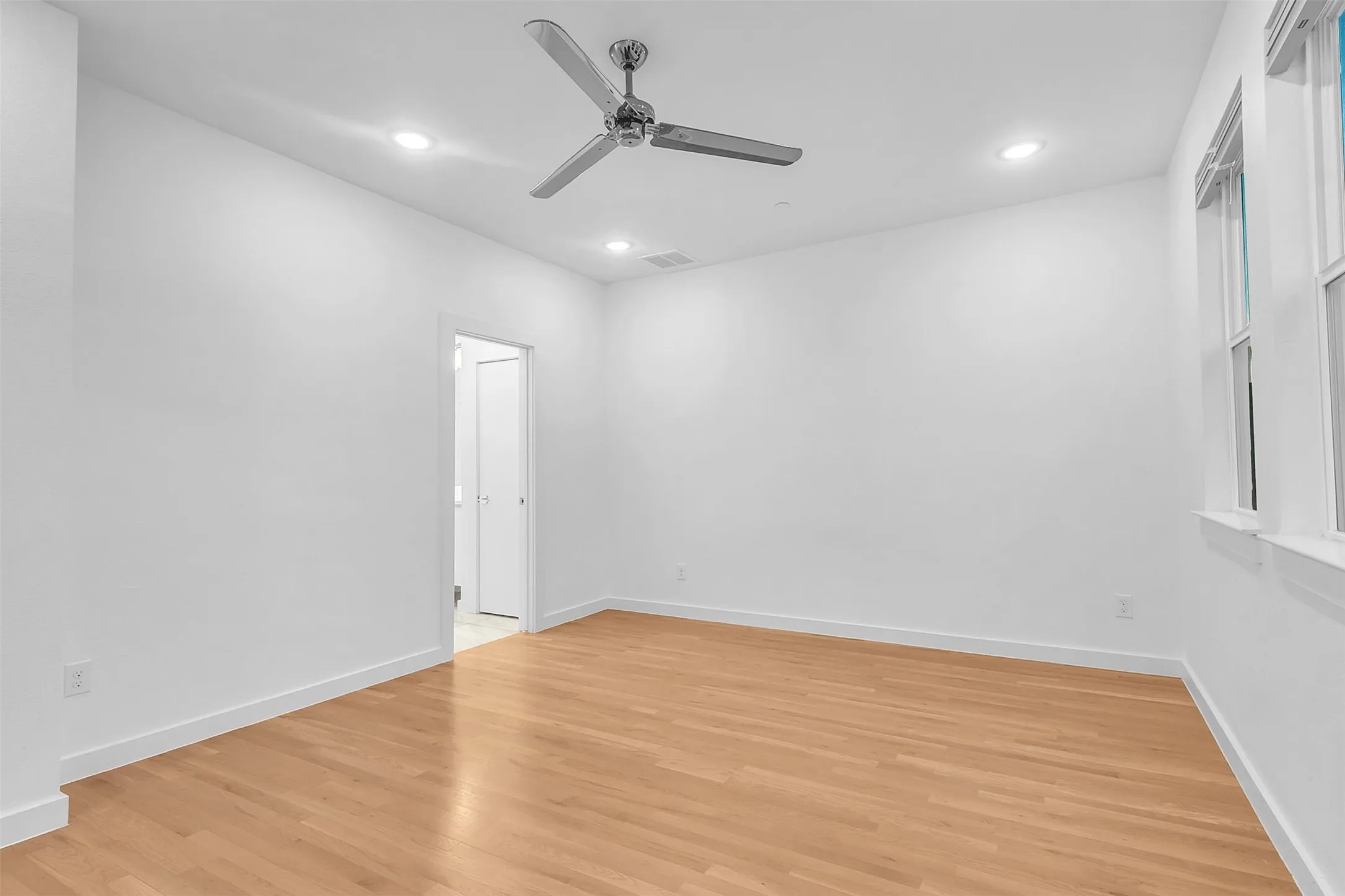 Bedroom view toward the doorway to the adjoining bath area, with recessed lights and a chrome ceiling fan