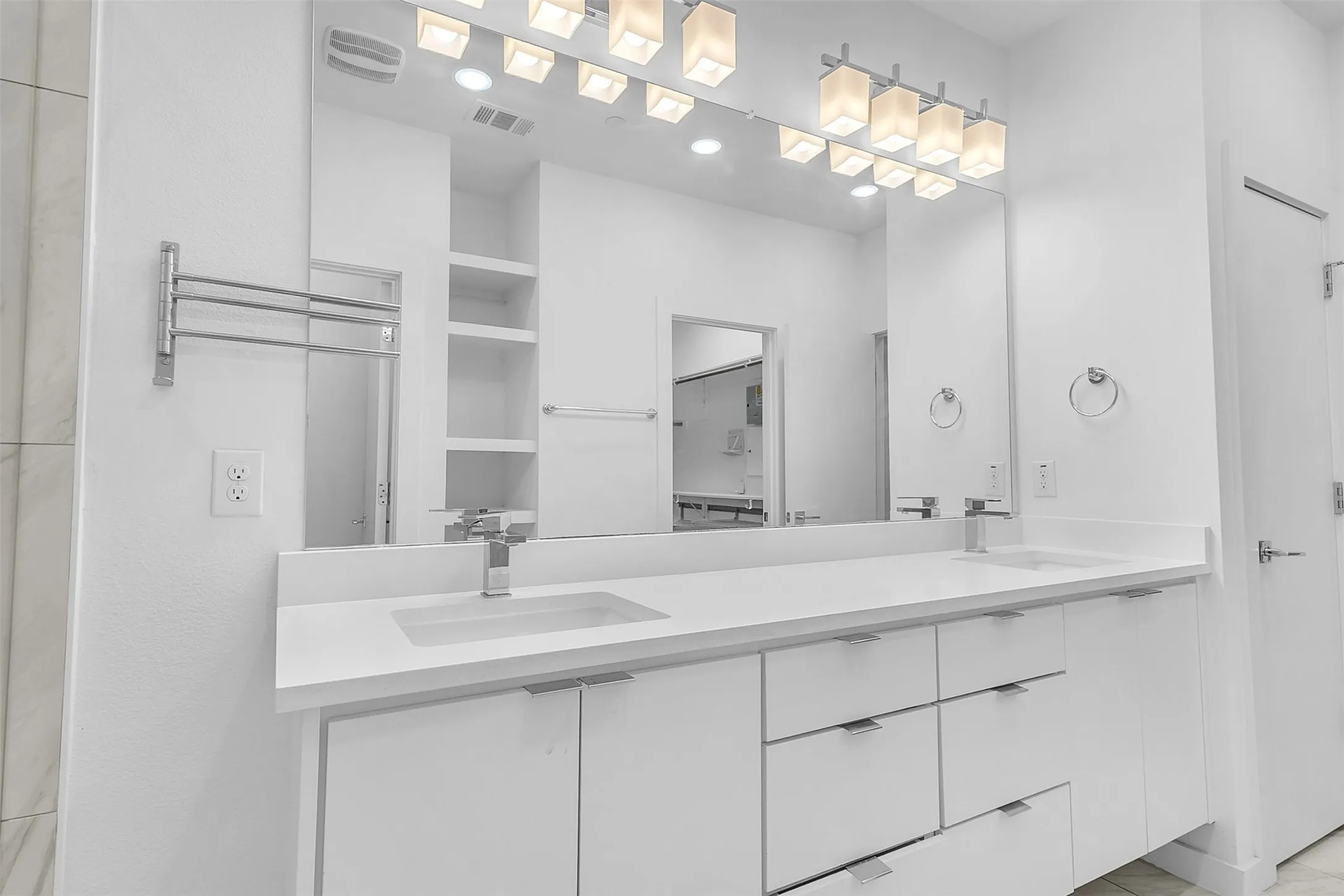 Primary bath in this Dallas condo with a long white vanity, dual undermount sinks, wide mirror and open shelving