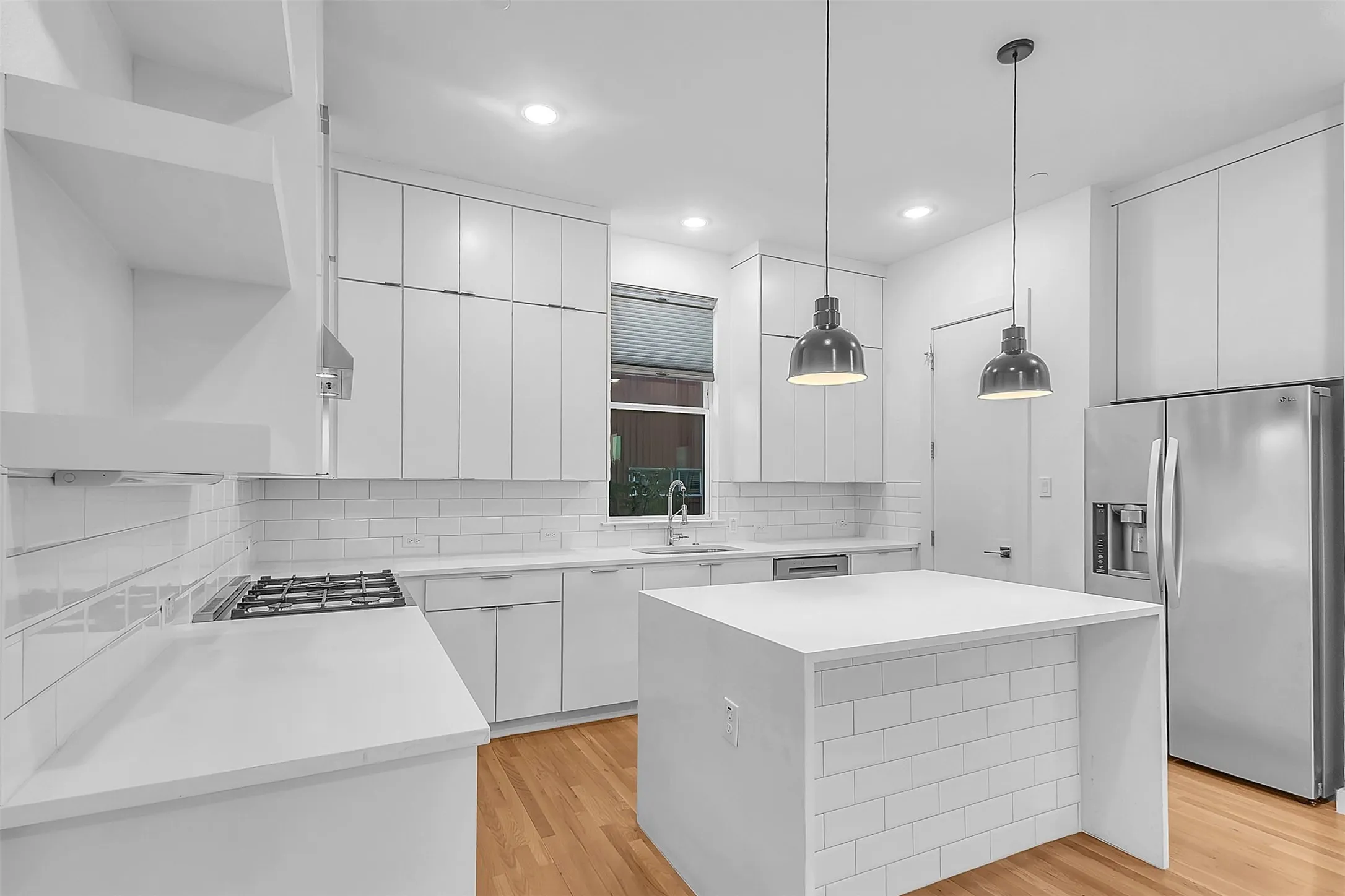 Kitchen in this Dallas condo with full-height white cabinets, waterfall island, gas range and stainless refrigerator