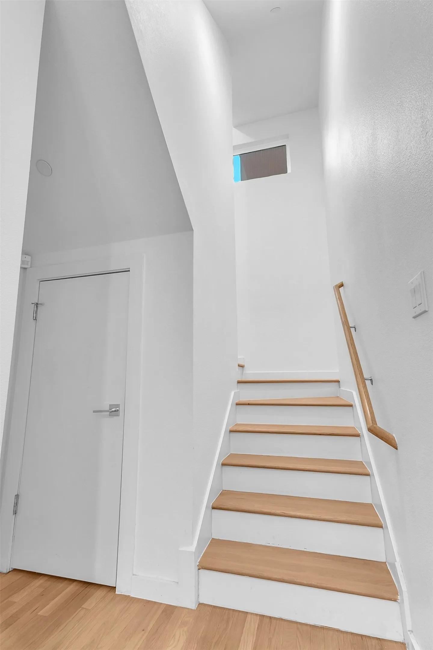 Staircase with wood treads, white risers and a wood handrail, with a hall door and a transom window above