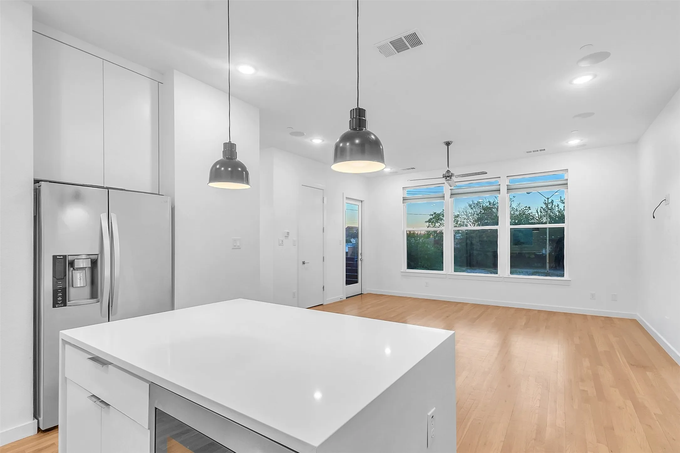 View from the kitchen island past the stainless refrigerator into the living area with a wall of windows