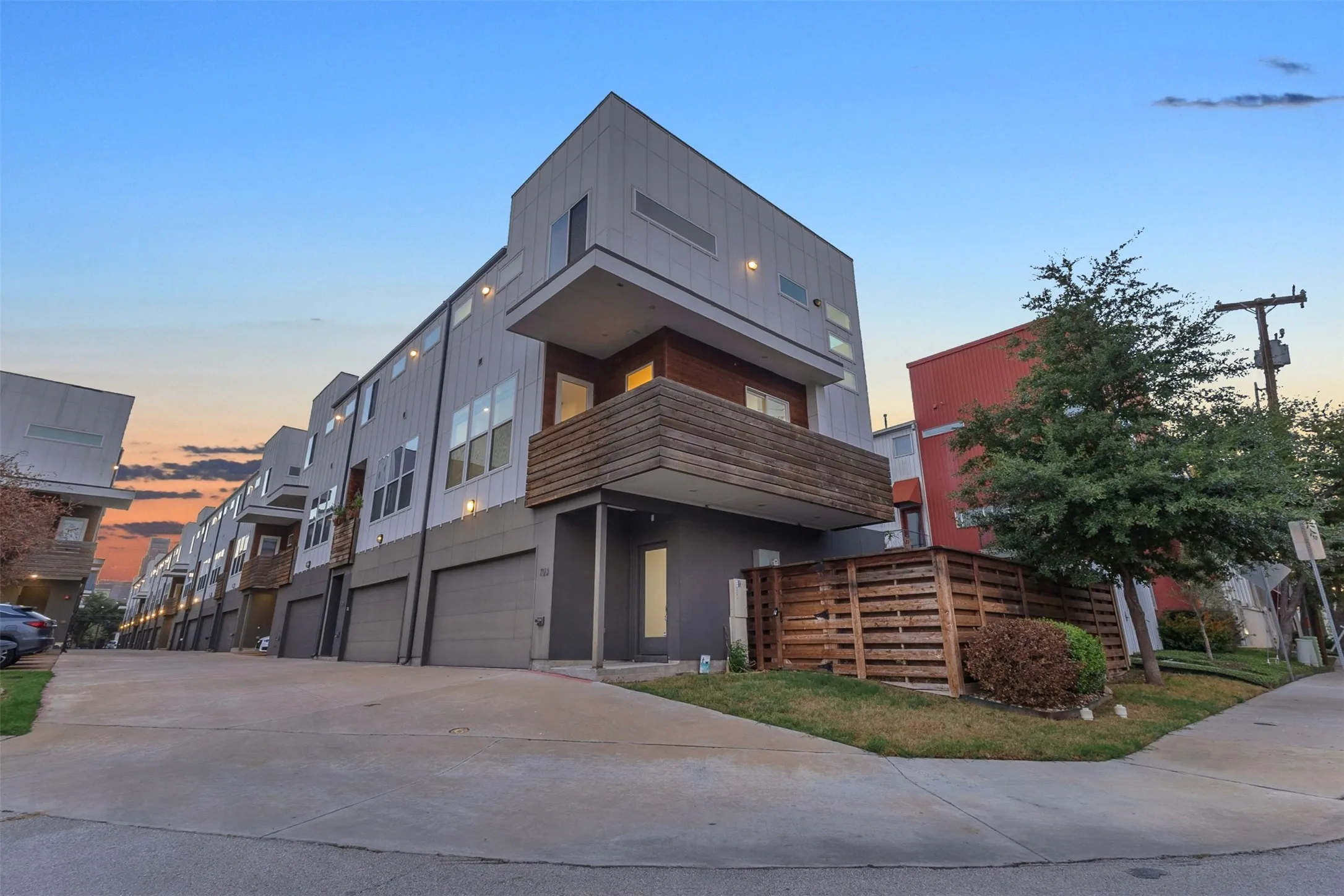 Wide view along the shared drive showing the corner condo, its fenced side yard and neighboring units at dusk