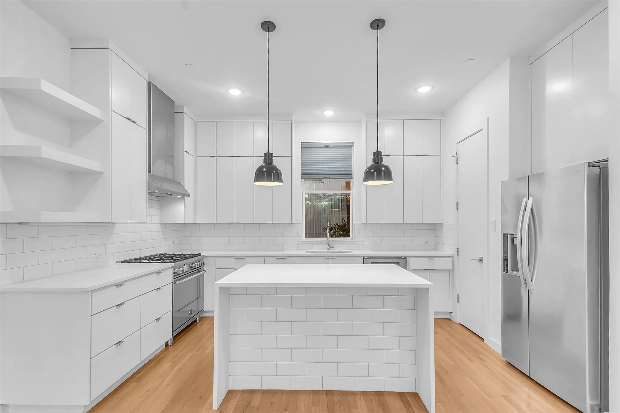 Straight-on view of the kitchen with two pendant lights over the waterfall island, open shelves and refrigerator