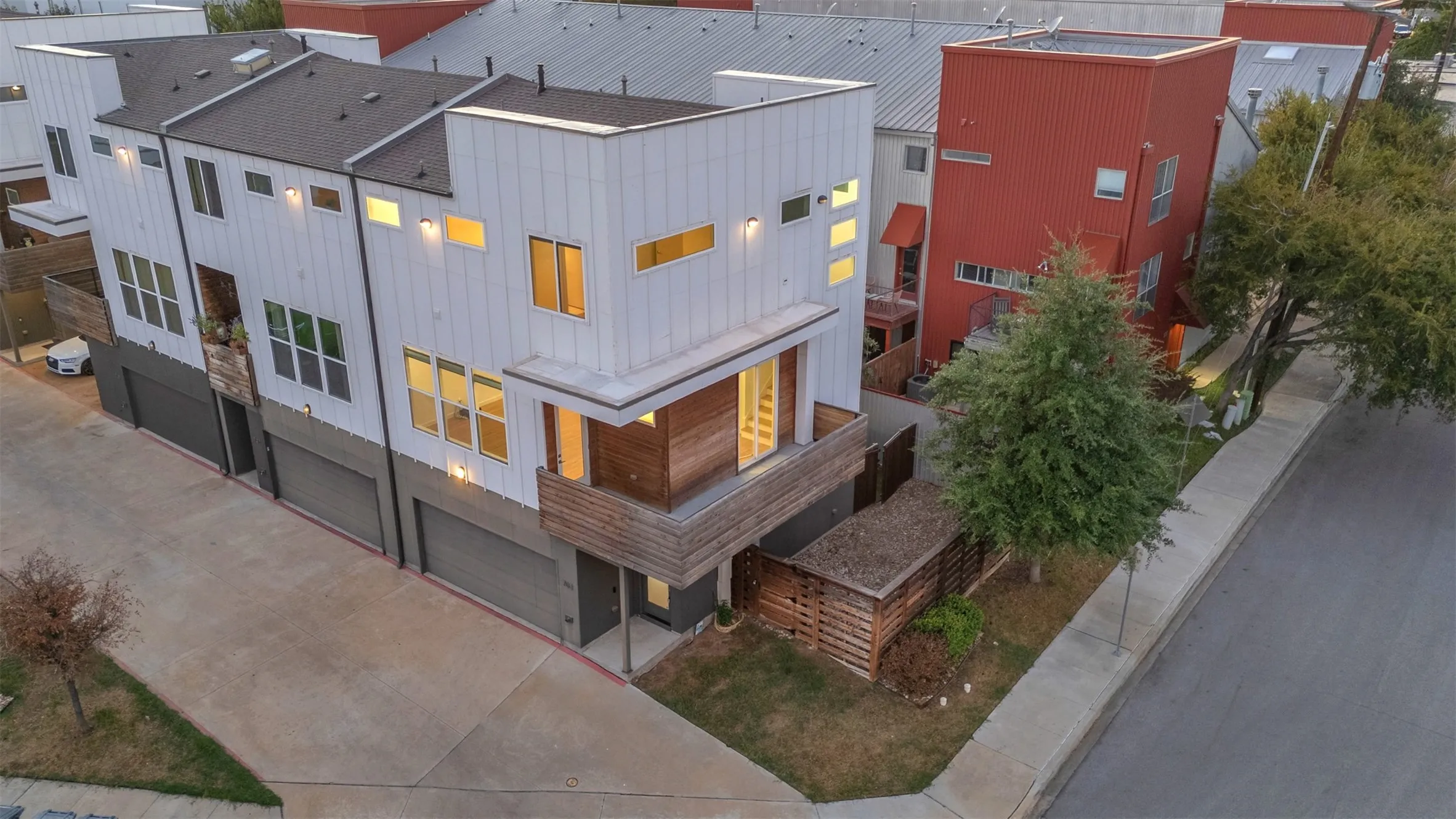 Overhead view of the corner unit at dusk with its wood balcony, front entry, 2-car garage and fenced side yard
