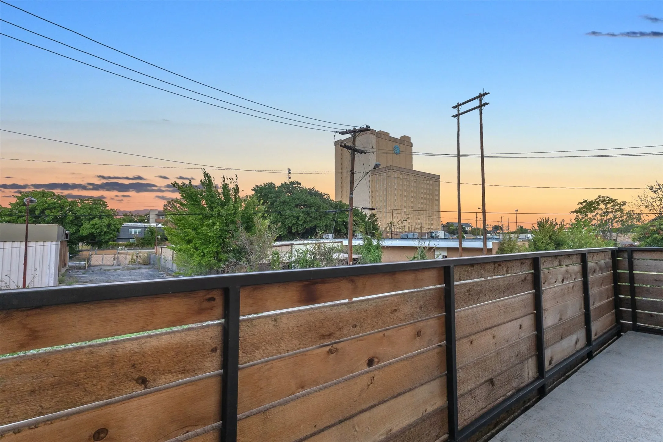 Corner of the wood-railed balcony at sunset, looking out over nearby rooftops and trees in East Dallas