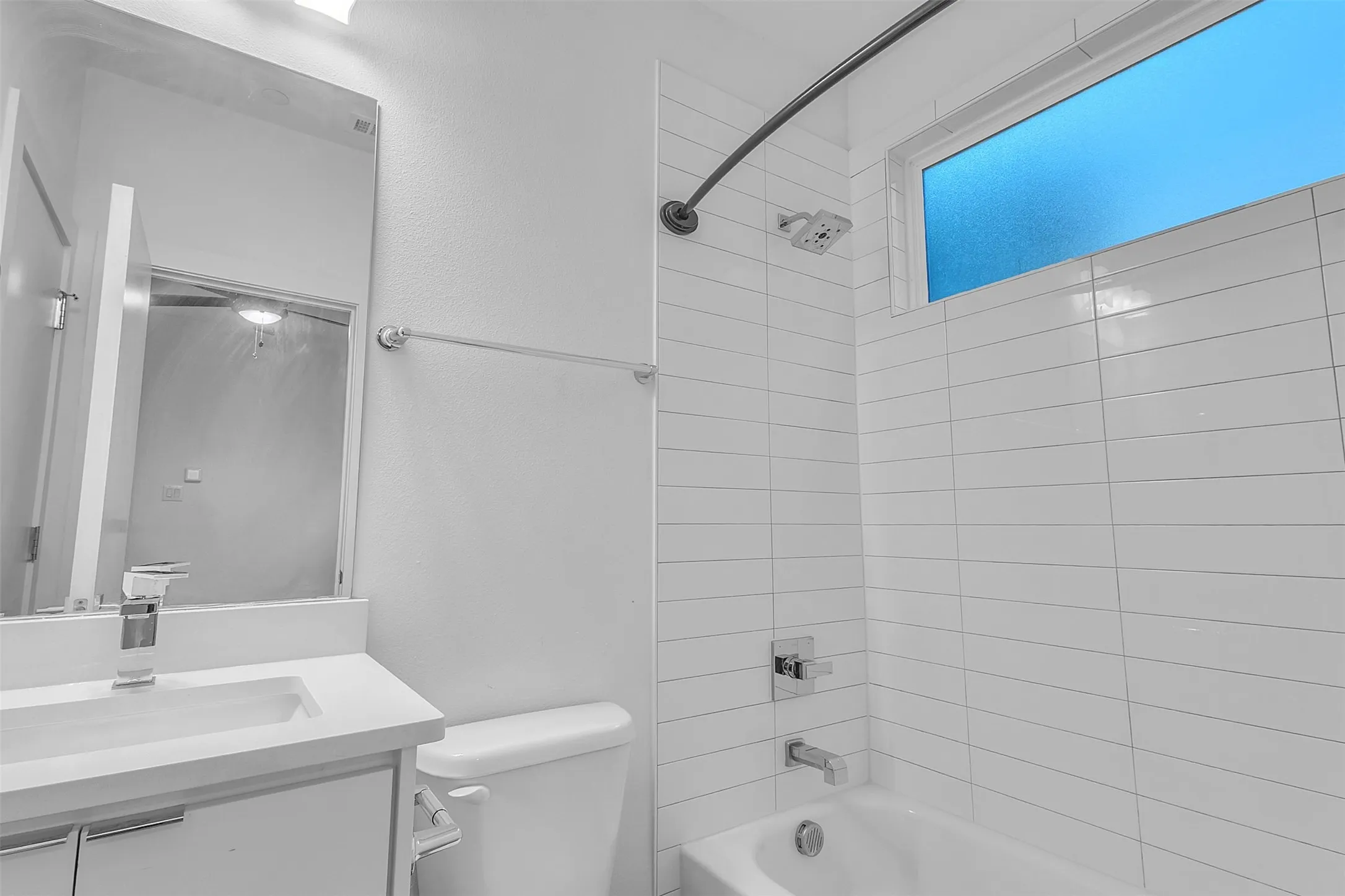 Secondary bath with a white vanity, tub and shower combo, tall white subway-style wall tile and a frosted window