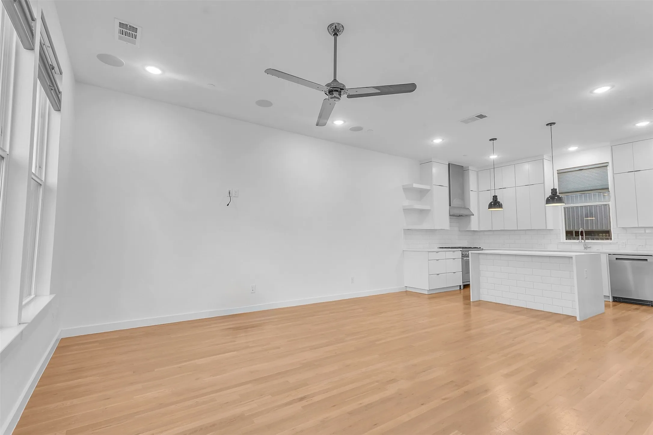 Living area looking toward the white kitchen, showing the open layout, recessed lighting and wood-look floors
