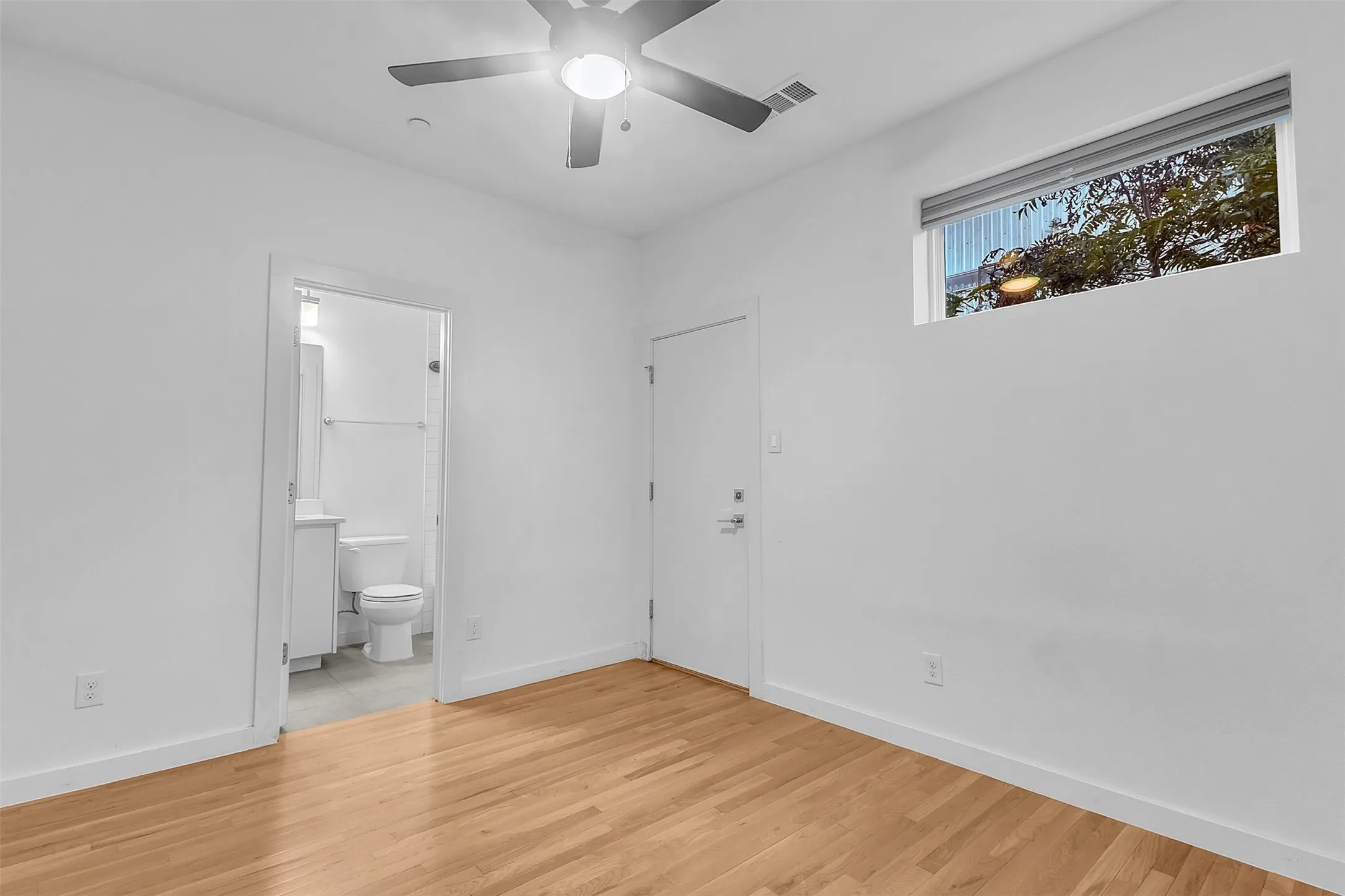 Bedroom with an en suite bath, a ceiling fan with light, a transom window with shade and wood-look floors