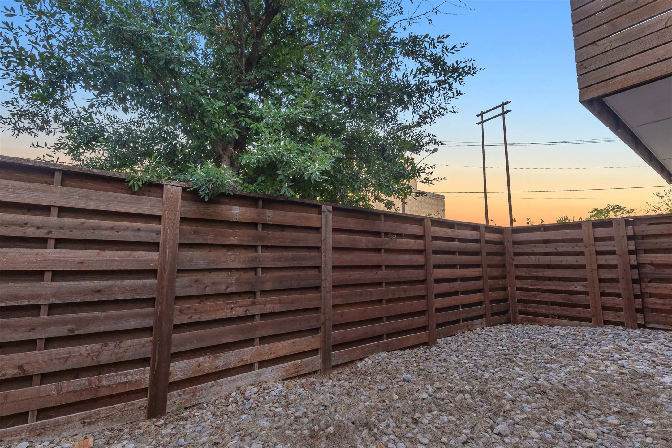 Fenced side yard with river rock ground cover, horizontal wood fencing and a mature tree overhead