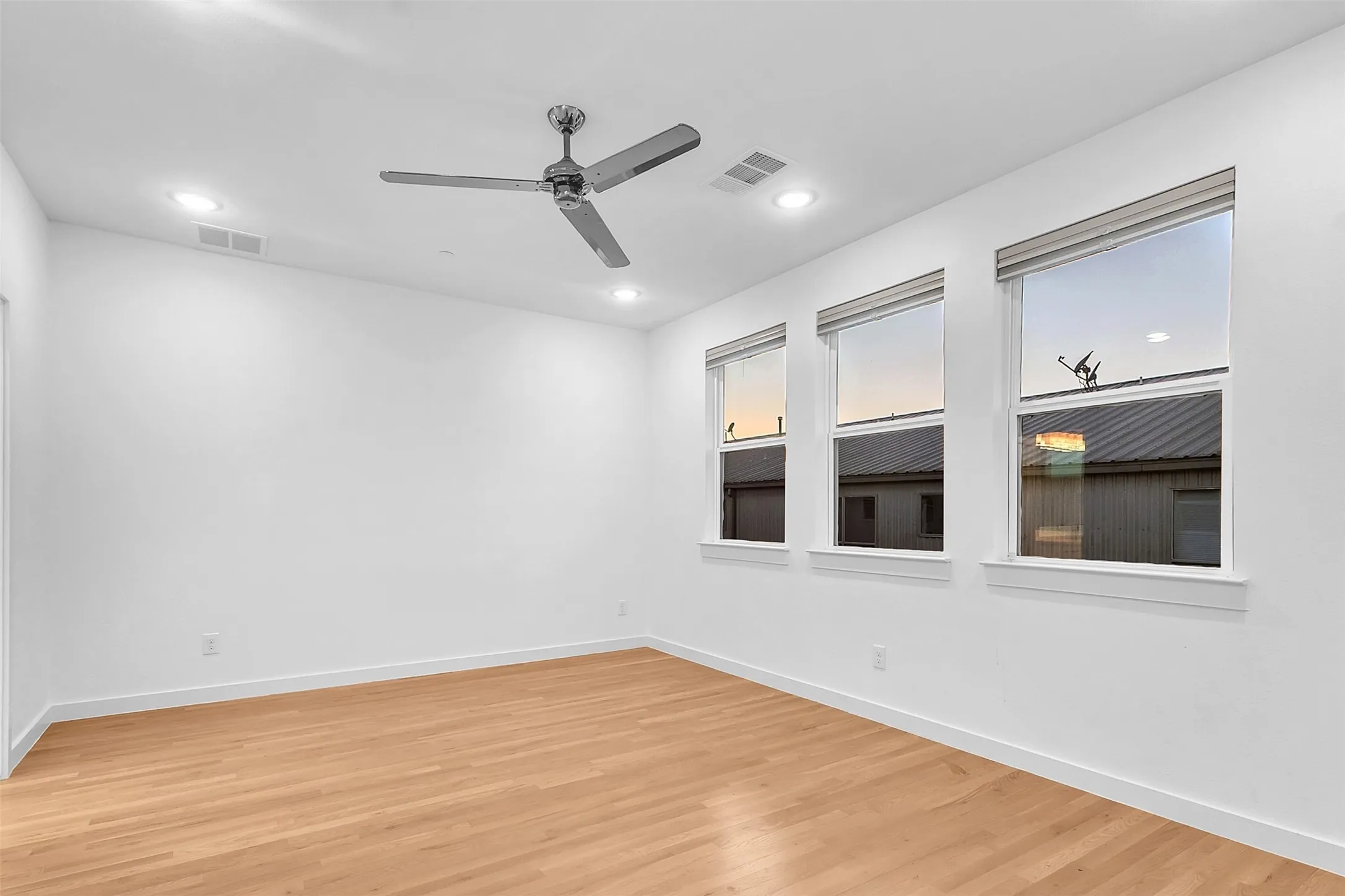 Spacious bedroom with three shaded windows, recessed lighting, a chrome ceiling fan and wood-look floors