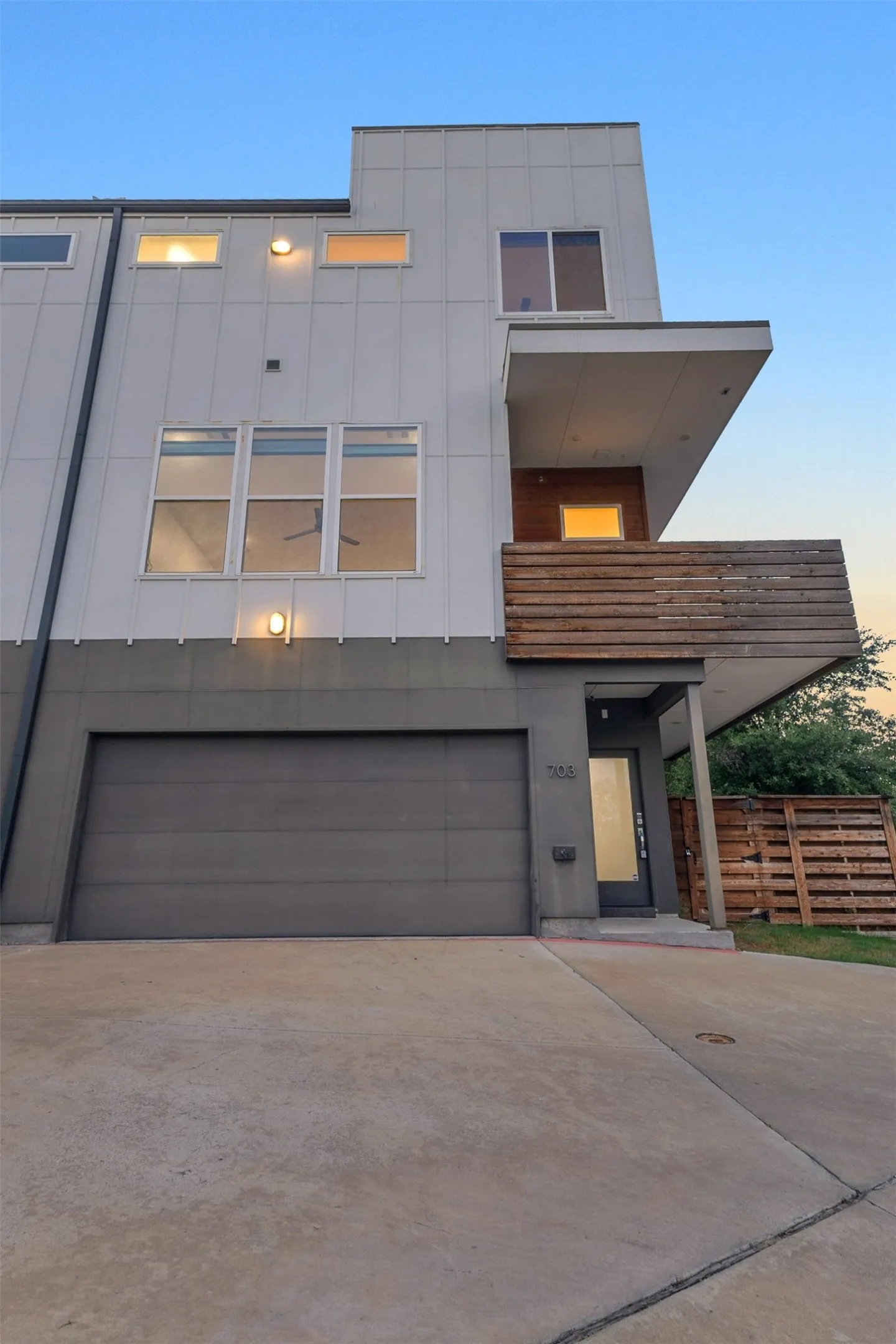 Front of unit 703 with a 2-car garage, glass front door, covered entry and wood balcony above, Dallas TX
