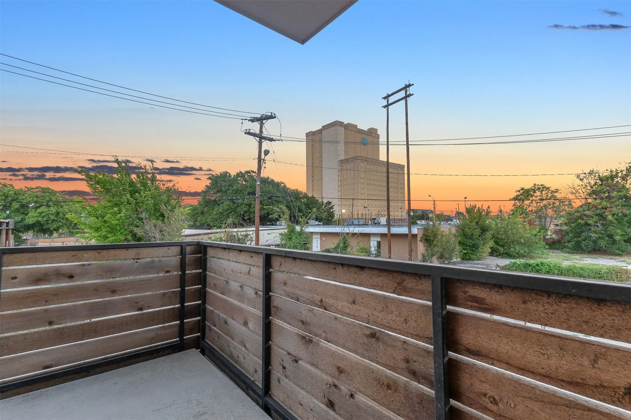 Wraparound balcony with horizontal wood rails, a concrete deck and open sunset views over the neighborhood