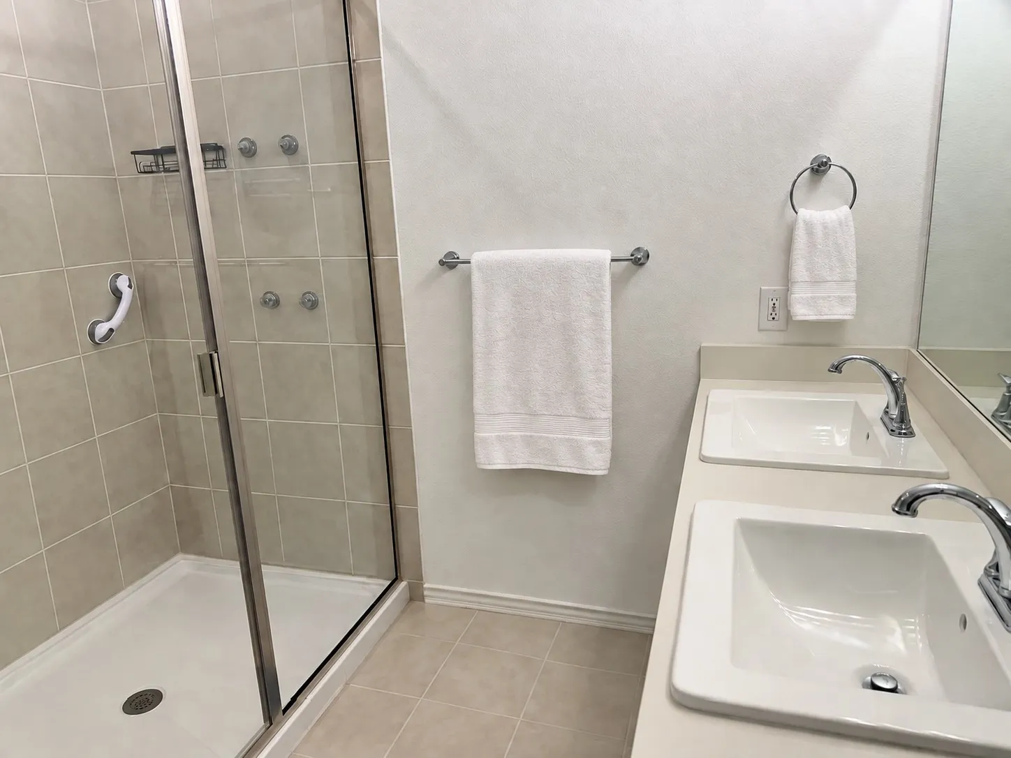 Glass-enclosed shower with a tiled surround, dual vanity with undermount sinks, chrome fixtures, and tiled flooring