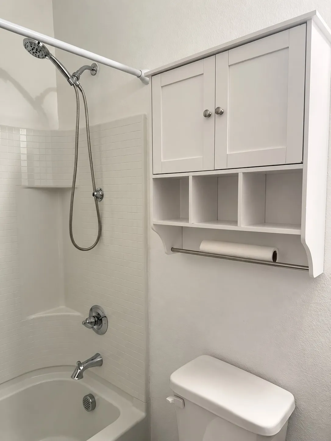 Bathtub with a handheld showerhead, chrome fixtures, and white tile surround