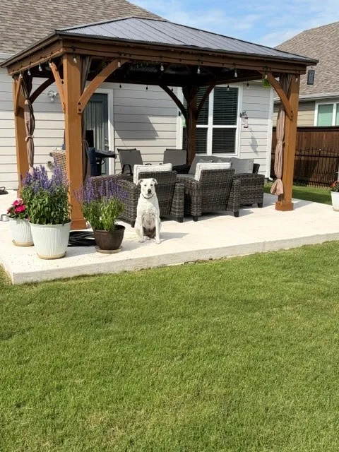 Covered outdoor patio with a concrete slab, wooden gazebo, and a manicured lawn